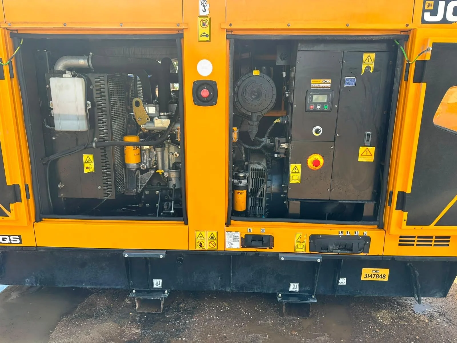 View of the engine compartment of a portable yellow JCB construction generator, showing various components, warning labels, and control panels.