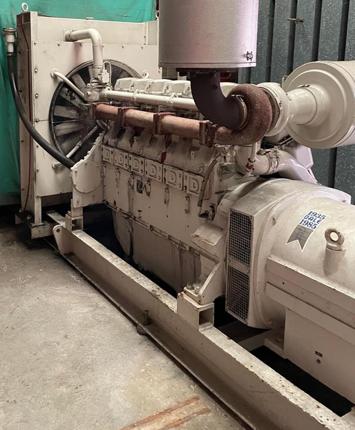 Industrial generator with exhaust pipe and cooling fan, mounted on a metal frame in a warehouse.