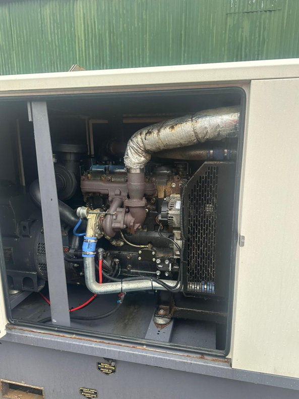 View of a generator engine inside a metal enclosure with visible pipes, hoses, and components.