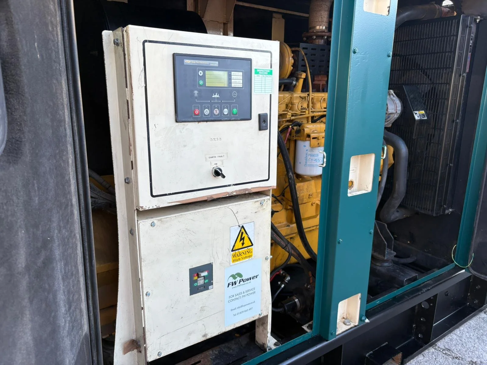 Close-up of an industrial generator with control panel, warning labels, and components.