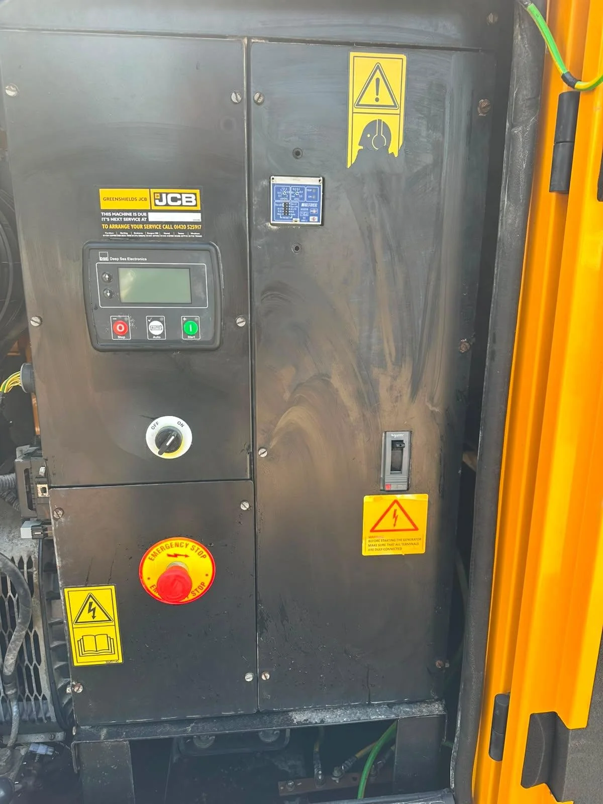 Electrical control panel with safety warning labels, emergency stop button, and digital display, mounted on industrial equipment.