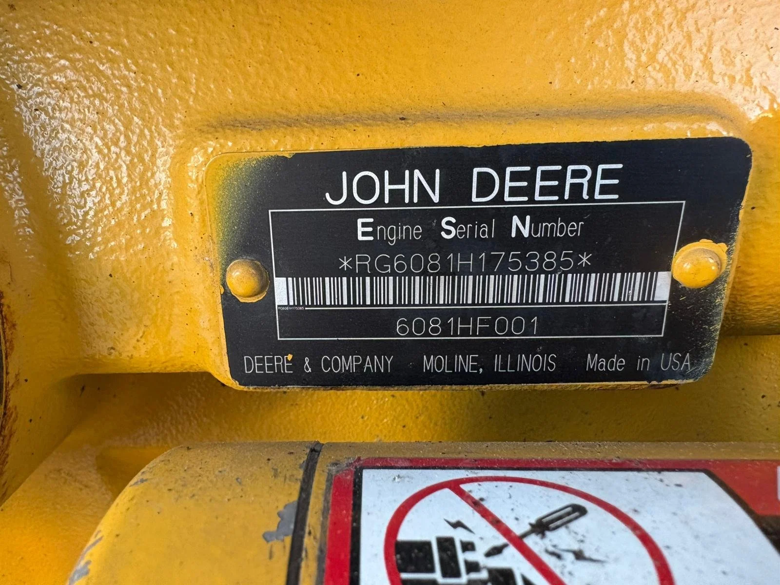 Close-up of a black and yellow John Deere machinery identification plate showing the engine serial number, located on yellow equipment.