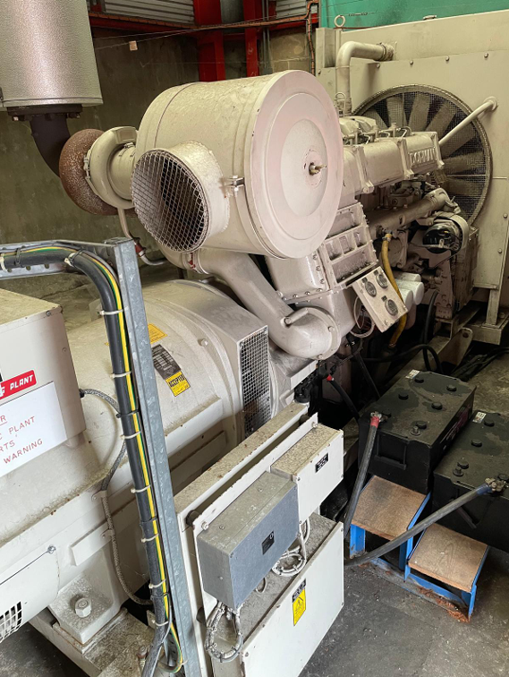 Large industrial generator or engine with various pipes, wires, and mechanical components in an industrial setting.