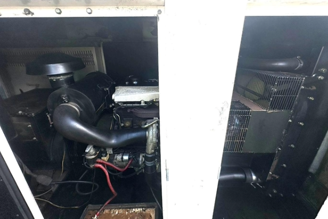 Interior view of electronic or mechanical equipment with black and metallic components, including a large black cylindrical part, a bent black pipe, and red wiring.
