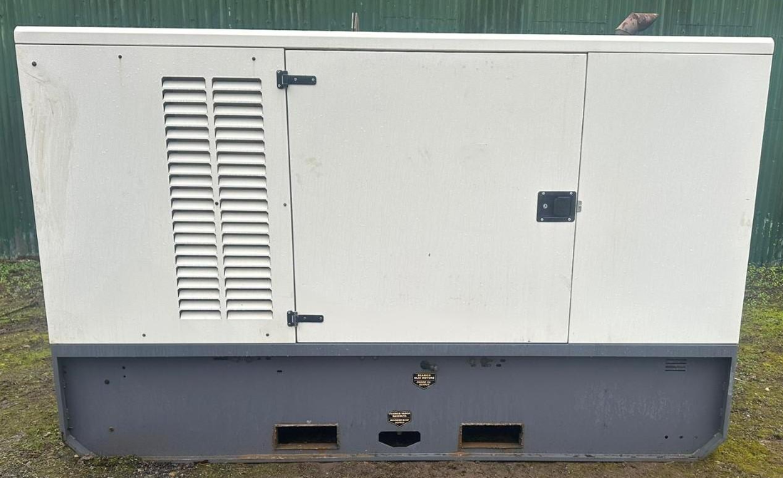 Large industrial generator outside on grass with a green fence in the background.