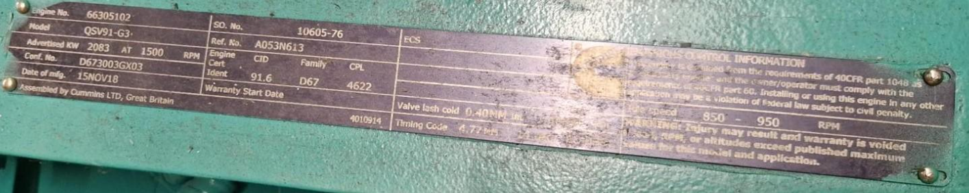 Close-up of a purple and silver engine data plate with technical specifications and serial numbers on a teal-green engine surface.