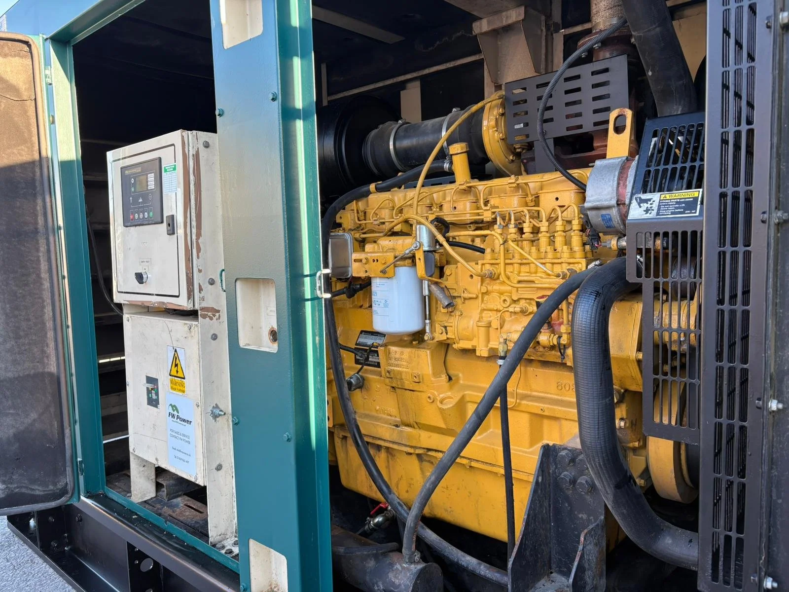 Close-up of a yellow industrial diesel engine inside a generator housing, with cables and various components visible.