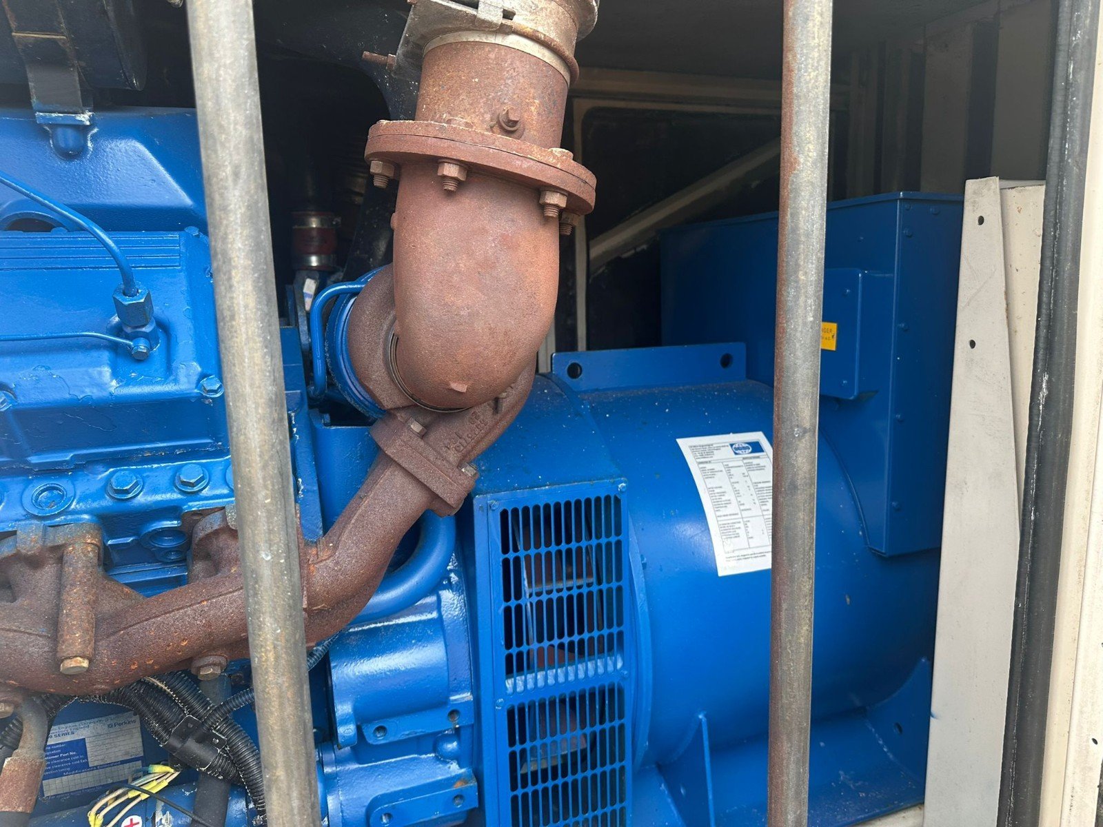 Close-up of a blue generator engine with a rusted exhaust pipe and surrounding metal bars.
