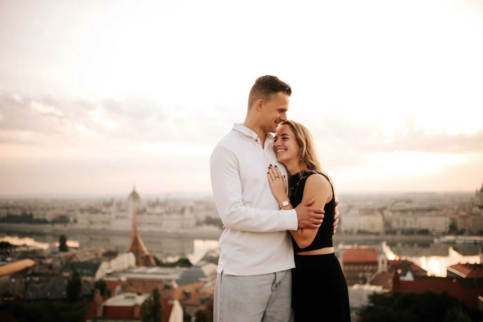 Couple embracing at sunrise with a panoramic Budapest view.