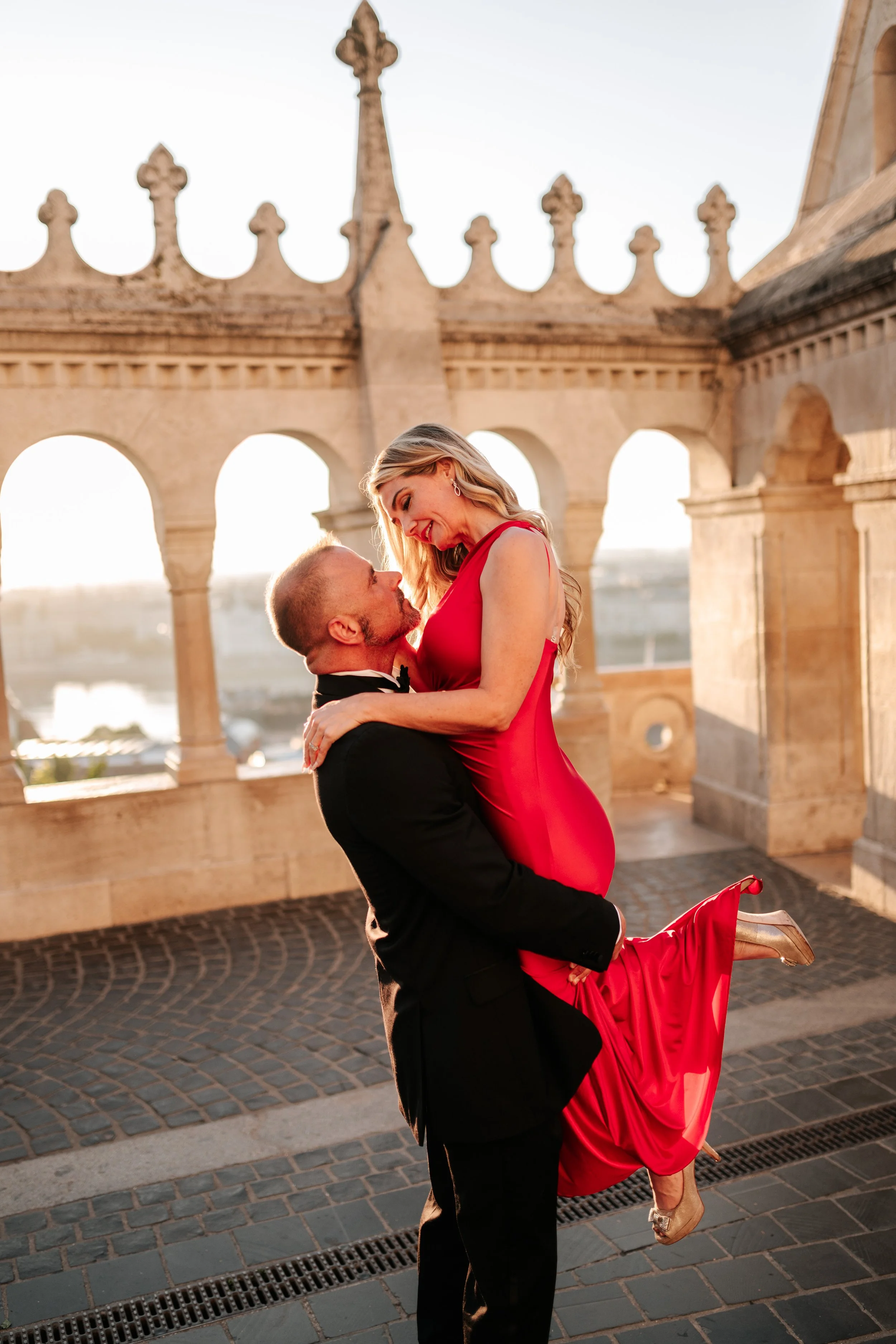 He lifts her beside the sunlit arches of Fisherman’s Bastion