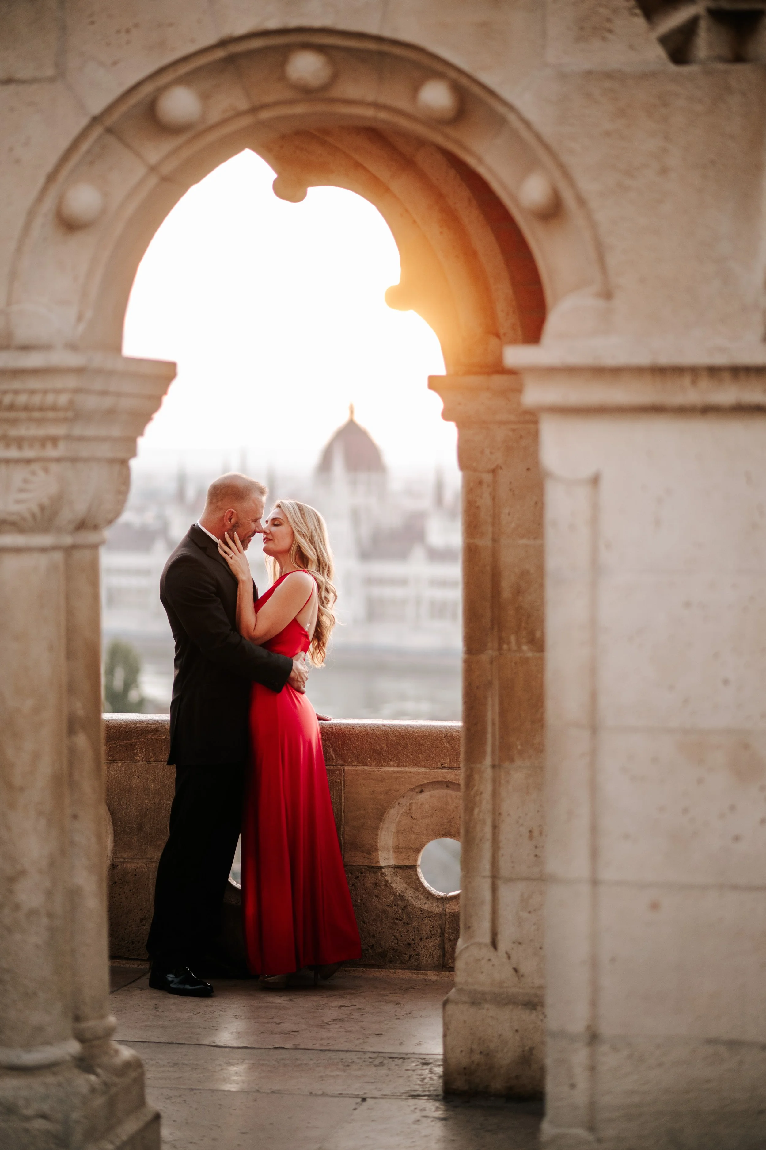 A kiss framed by a carved stone arch, with Parliament in the distance