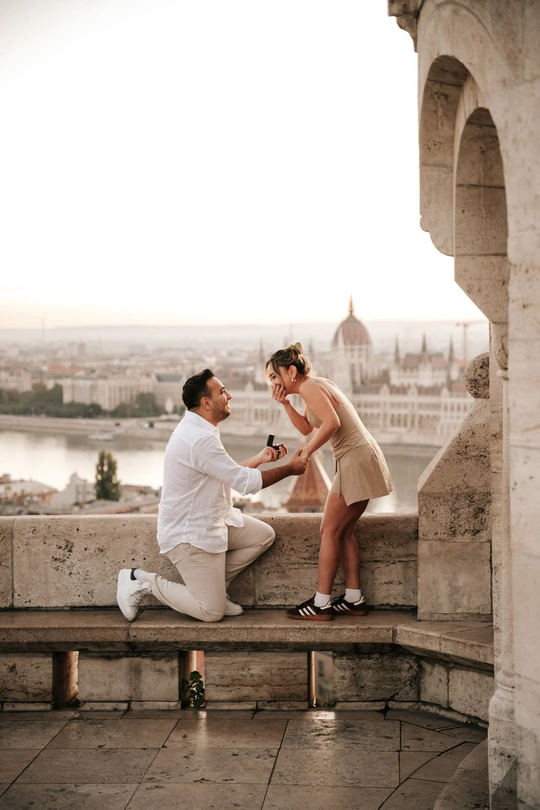 Man proposing at Fisherman’s Bastion with Budapest Parliament behind them at sunrise.