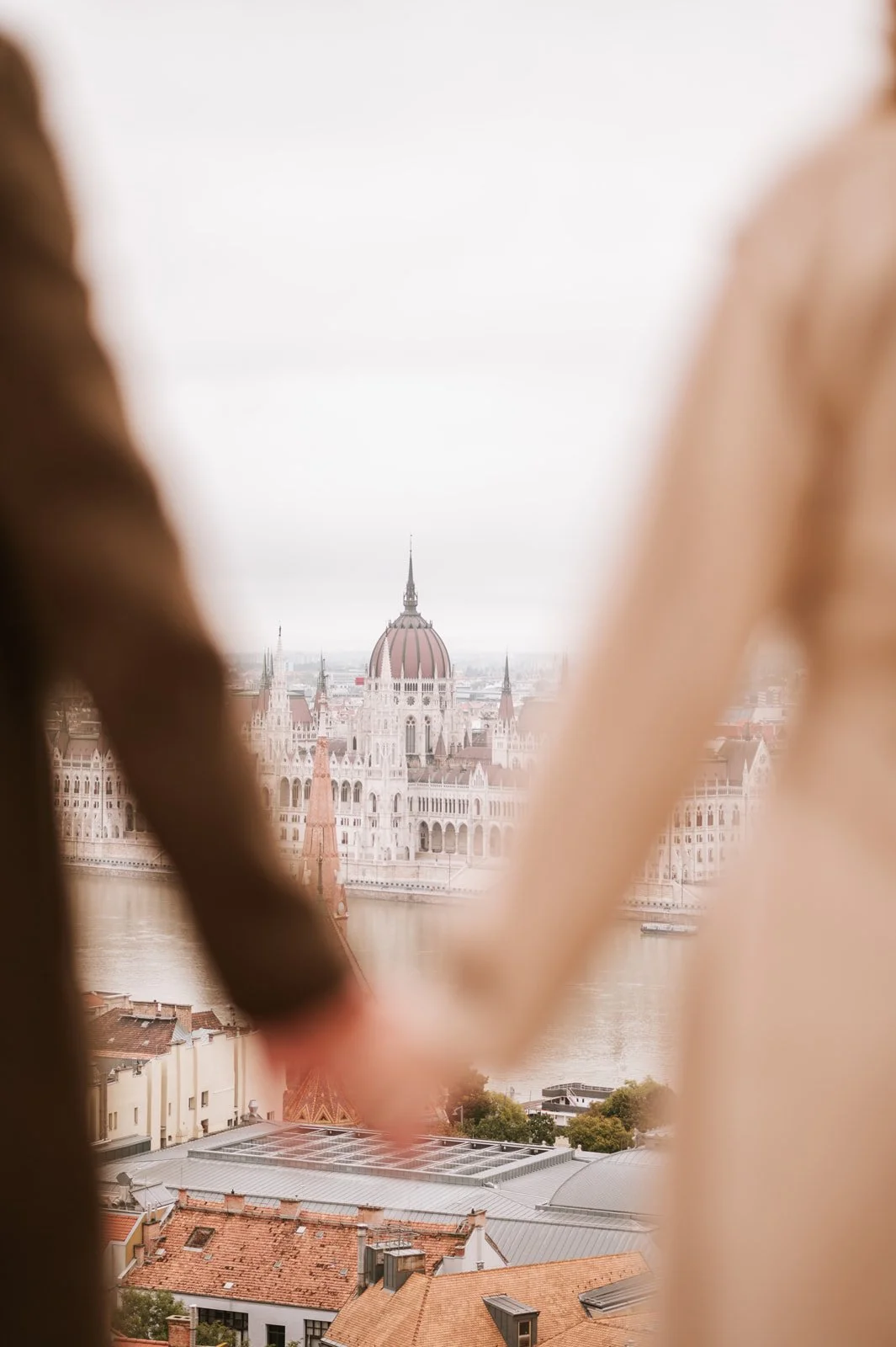 Couple holding hands with a soft view of the Budapest Parliament in the background.