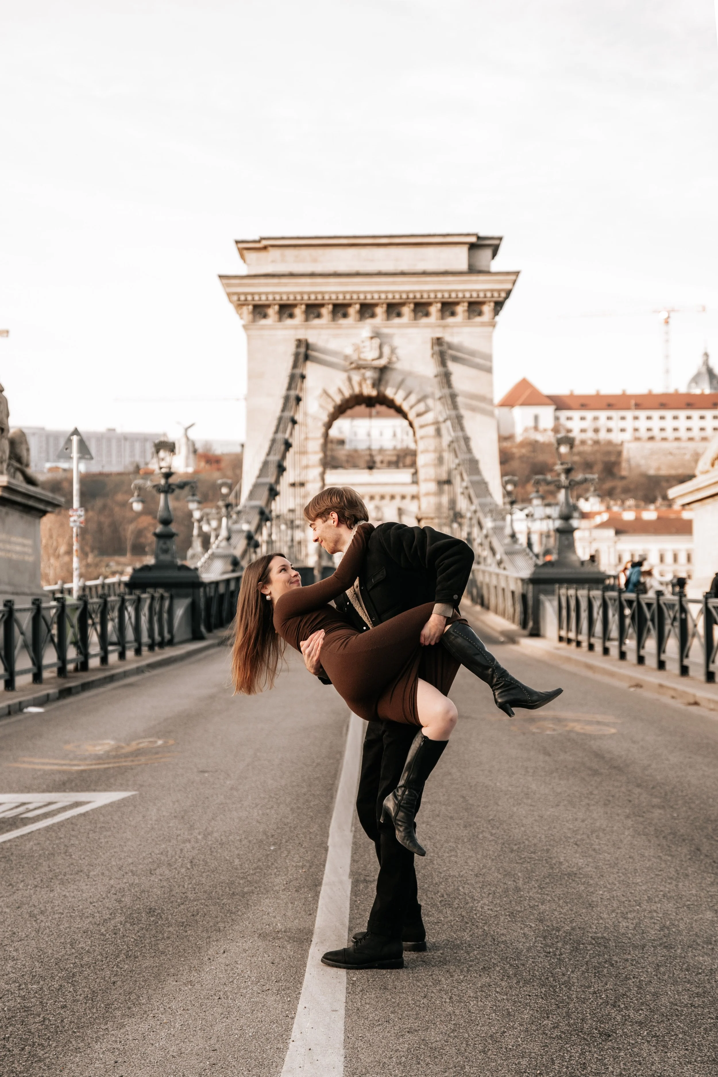 A couple dancing on a bridge near a large historic arch in Budapest, Hungary.