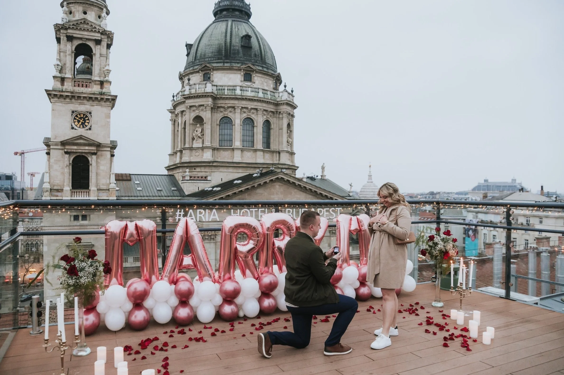 “Marry Me” rooftop proposal with balloon decor and St. Stephen’s Basilica in the background — elegant engagement in Budapest’s city center.