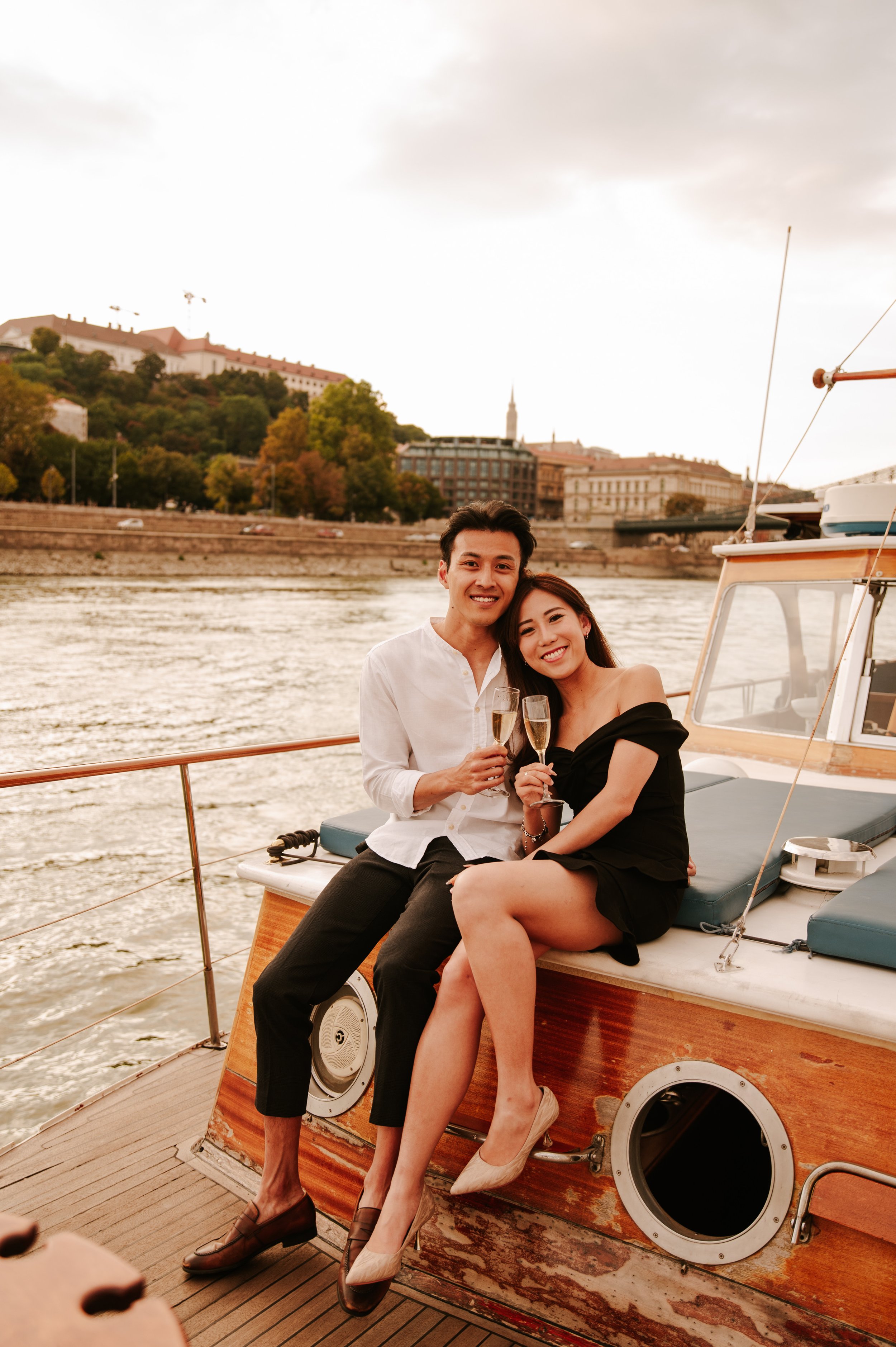 asian couple celebrating budapest engagement with champagne on private yacht
