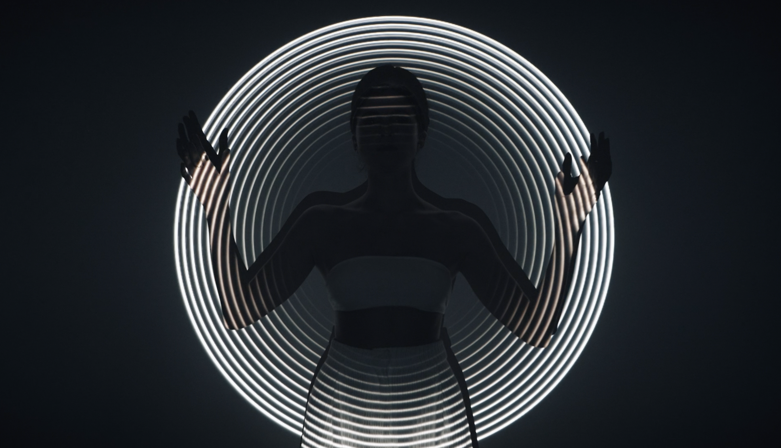 Silhouette of a woman standing in front of a circular LED light installation, with her hands raised, creating a symmetrical pattern.