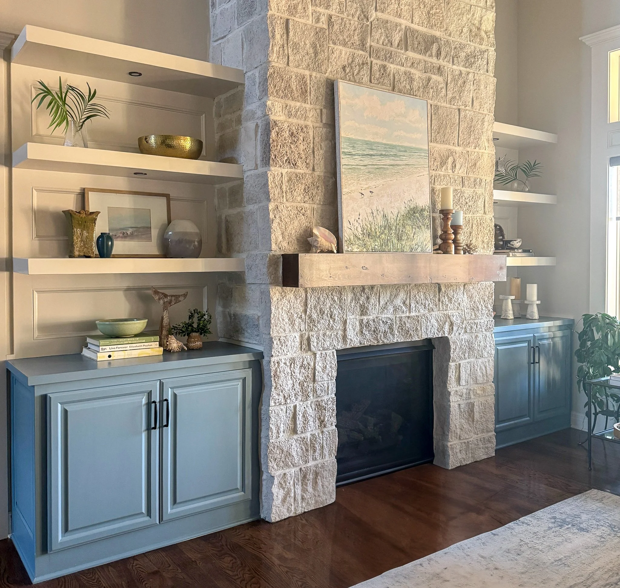 Living room with a stone fireplace, two built-in blue cabinets on either side, and decorative items like vases, books, and artwork on the shelves and mantel.