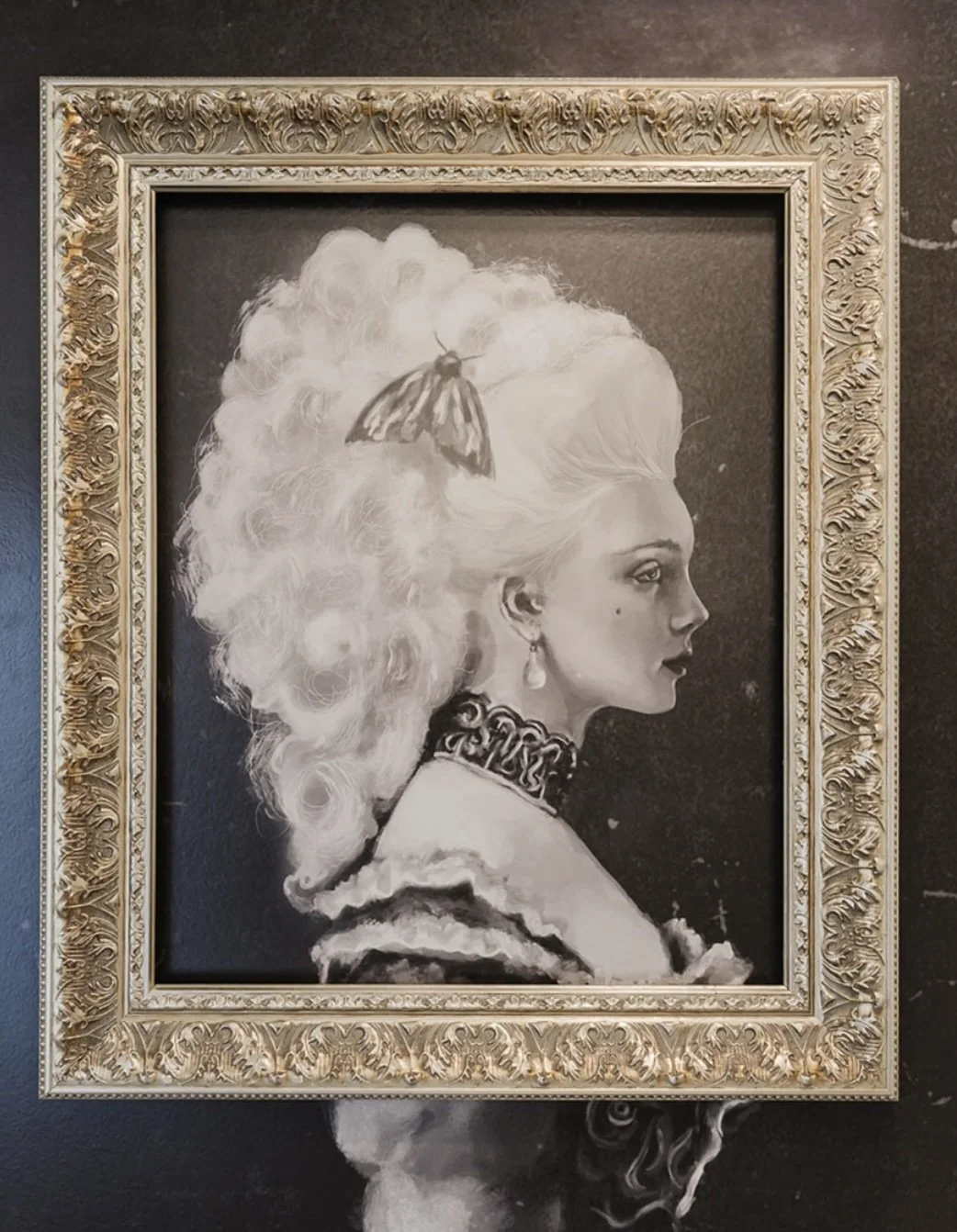A black and white portrait of a woman with large, curly hair, wearing vintage jewelry, framed in an ornate gold frame.