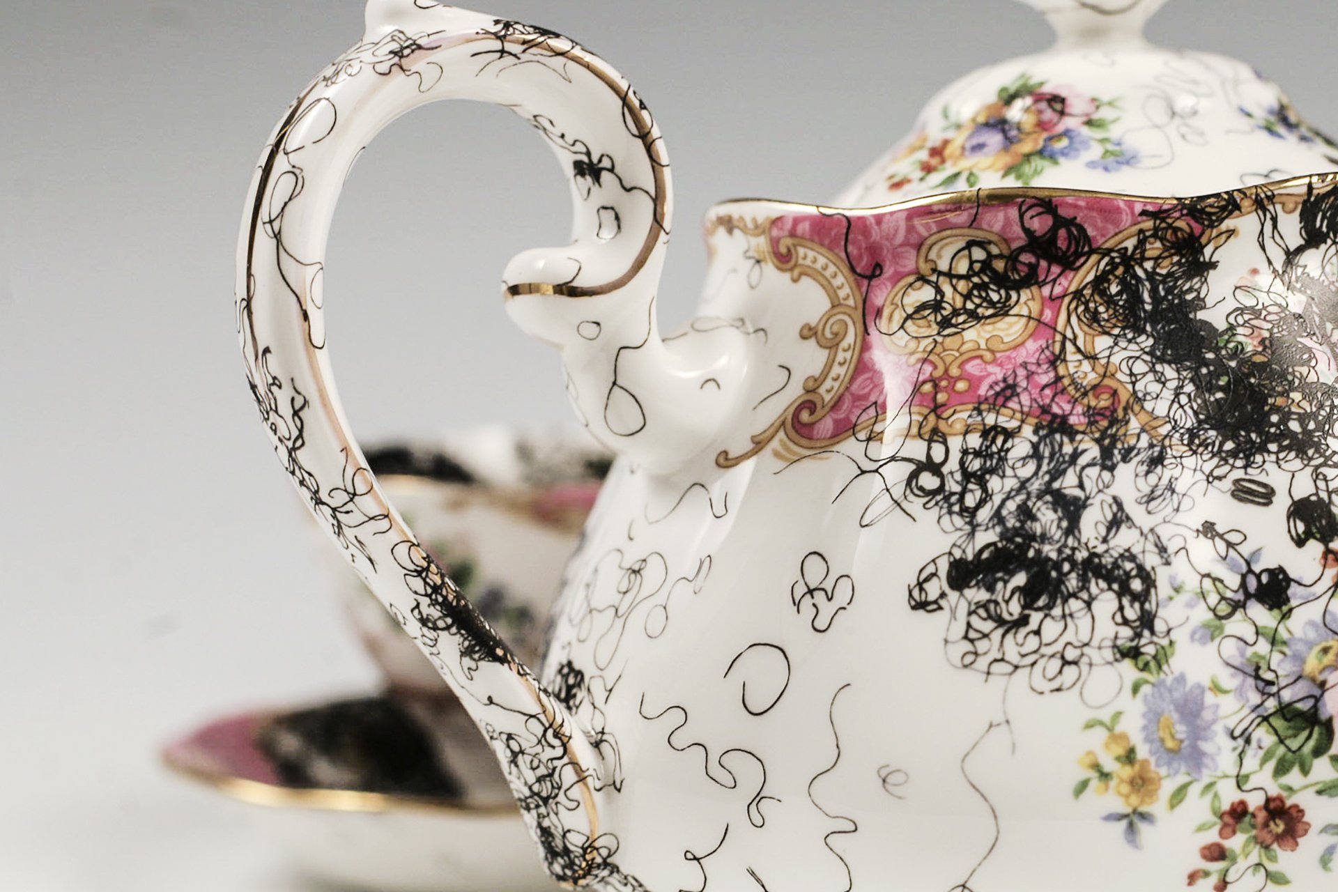 A vintage, china teapot and two cups and saucers with floral decorations is overlaid with decal drawings of curly, black hair. (Copy)