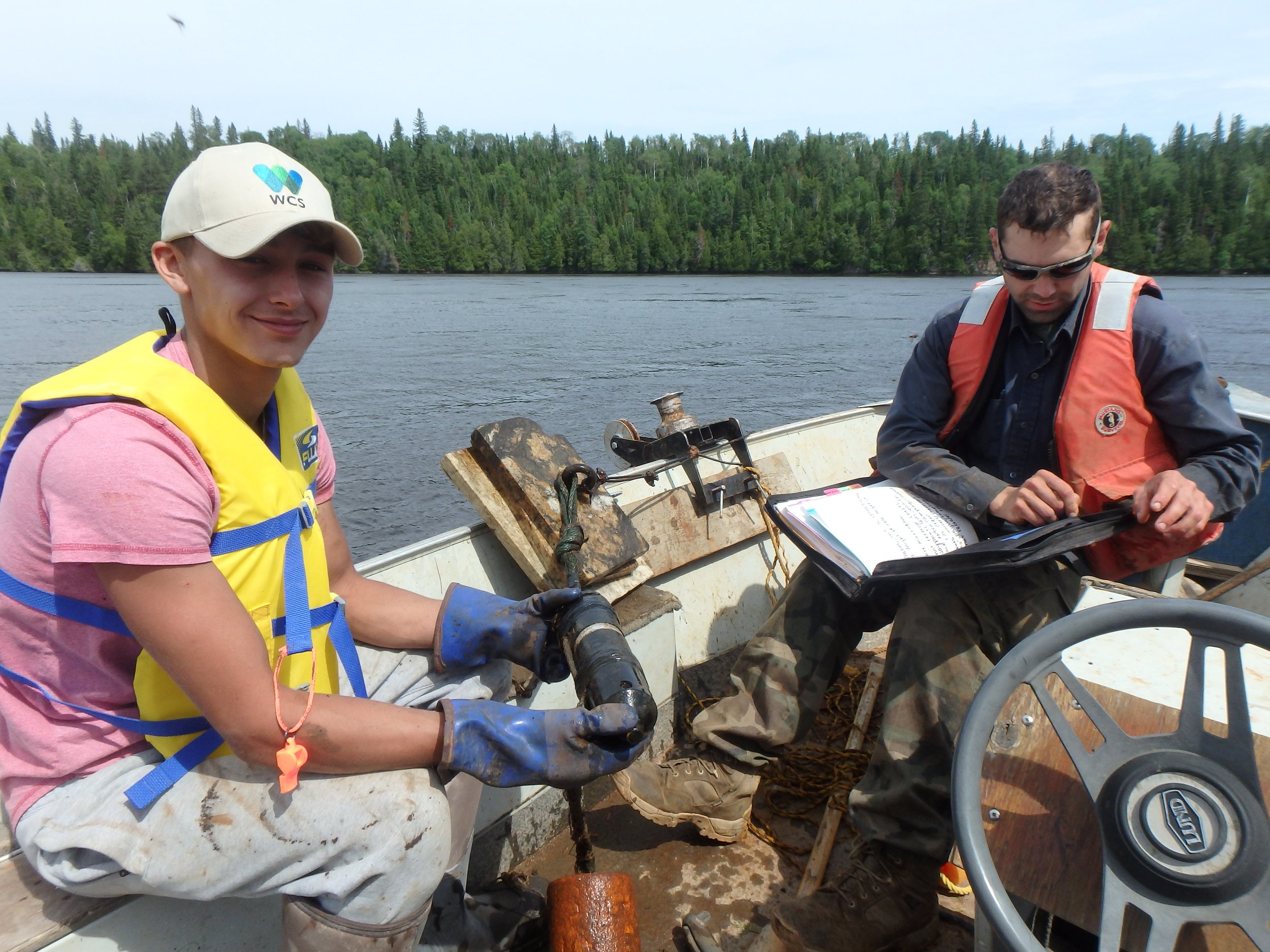 Justin Simard (left, MCFN youth) holds one of our underwater receivers that listen for tagged lake sturgeon. Jacob Seguin (WCS Canada) prepares equipment to keep the receivers working.