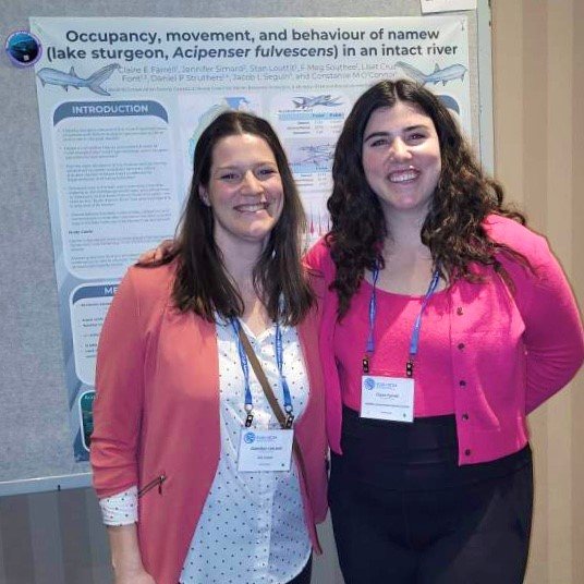  Gretchen Lescord (left) and Claire Farrell (right) hang out in front of a poster about the Learning from Lake Sturgeon program and the North French River! 