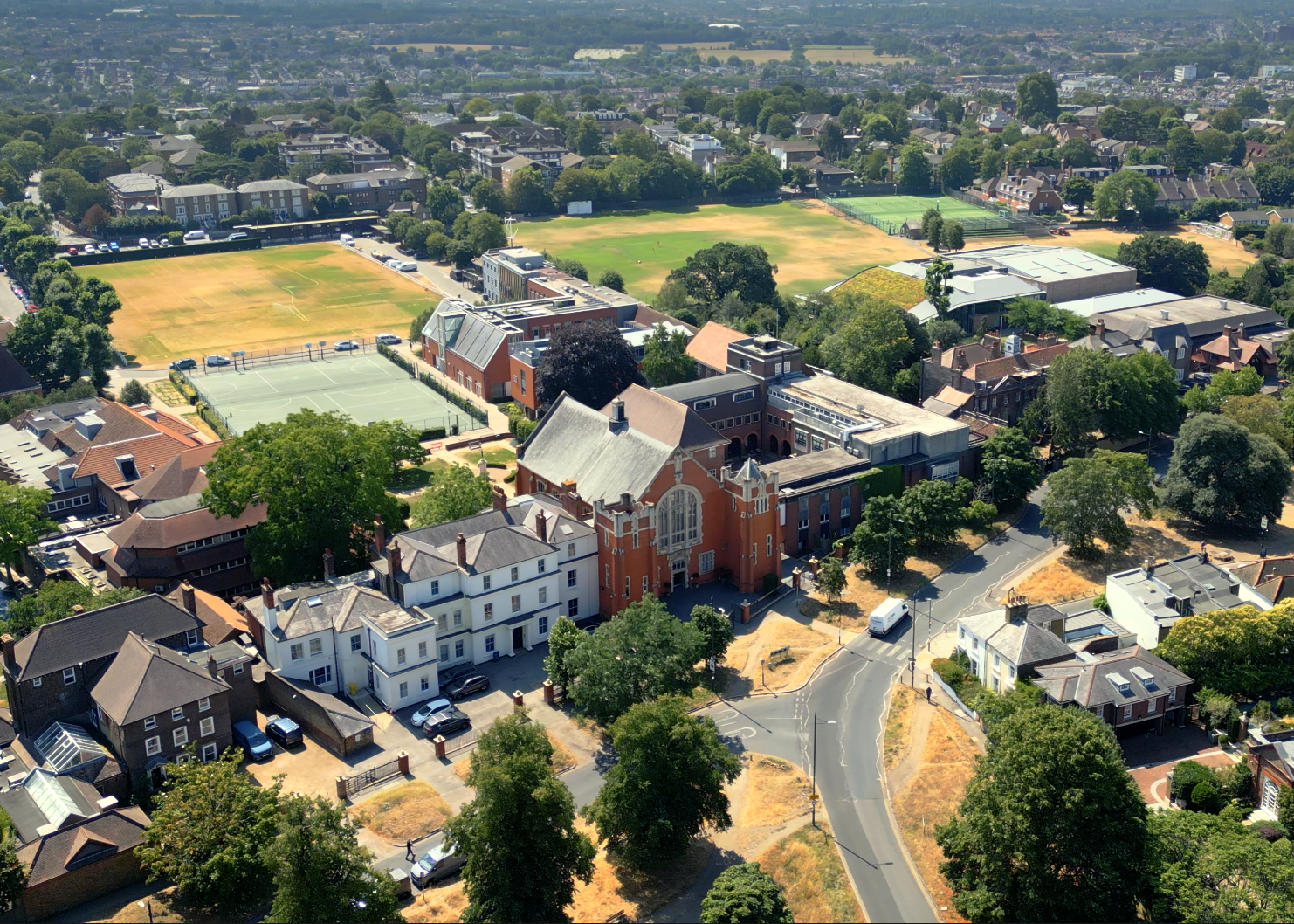 Aerial view of a neighborhood with university or college campus buildings, sports fields, tennis courts, and trees