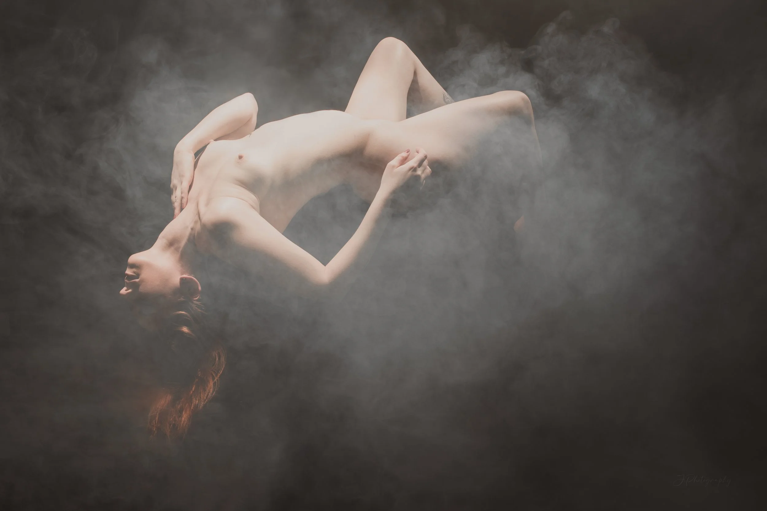 Une femme nue allongée sur le sol dans une ambiance brumeuse et sombre.