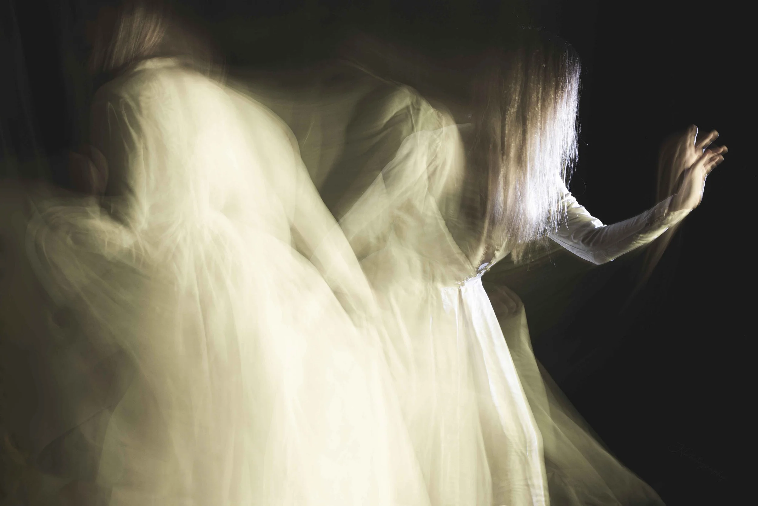 Une personne en robe blanche se déplaçant rapidement, créant un effet de mouvement flou.