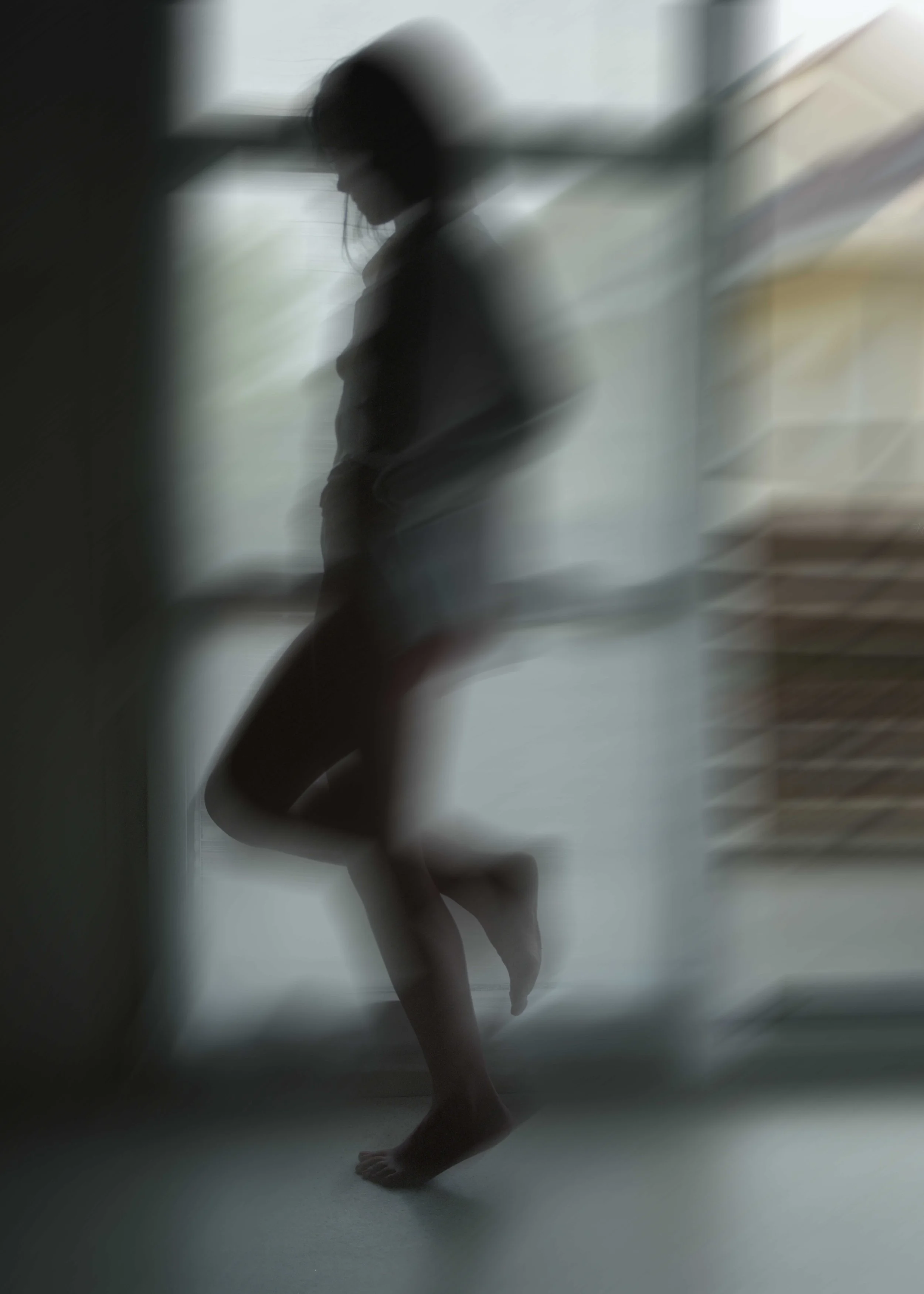 Silhouette floue d'une personne debout, vue de profil, dans un environnement intérieur avec fenêtres.