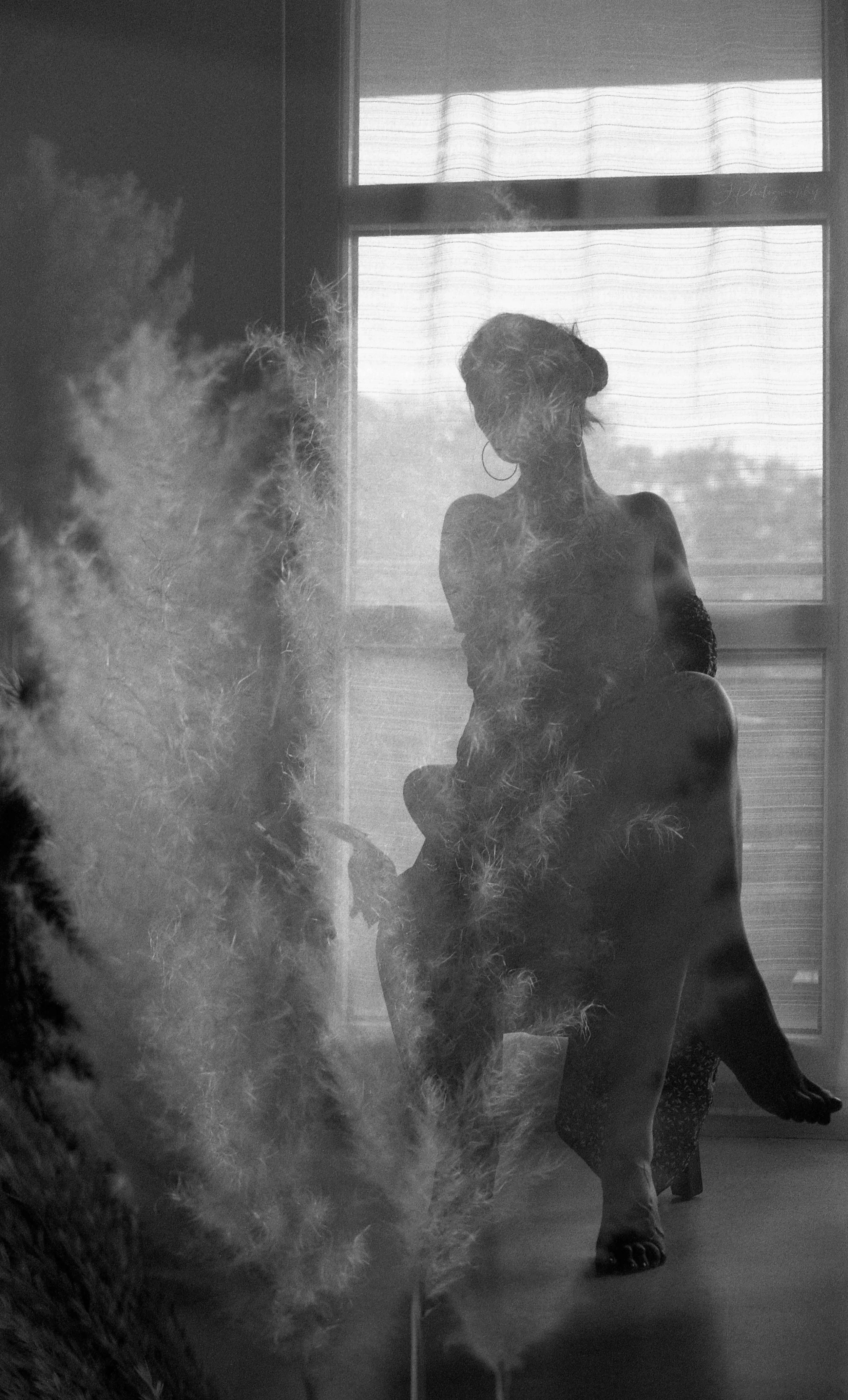 Silhouette d'une femme assise près d'une fenêtre avec des rideaux, photographie en noir et blanc, ambiance douce et mystérieuse.