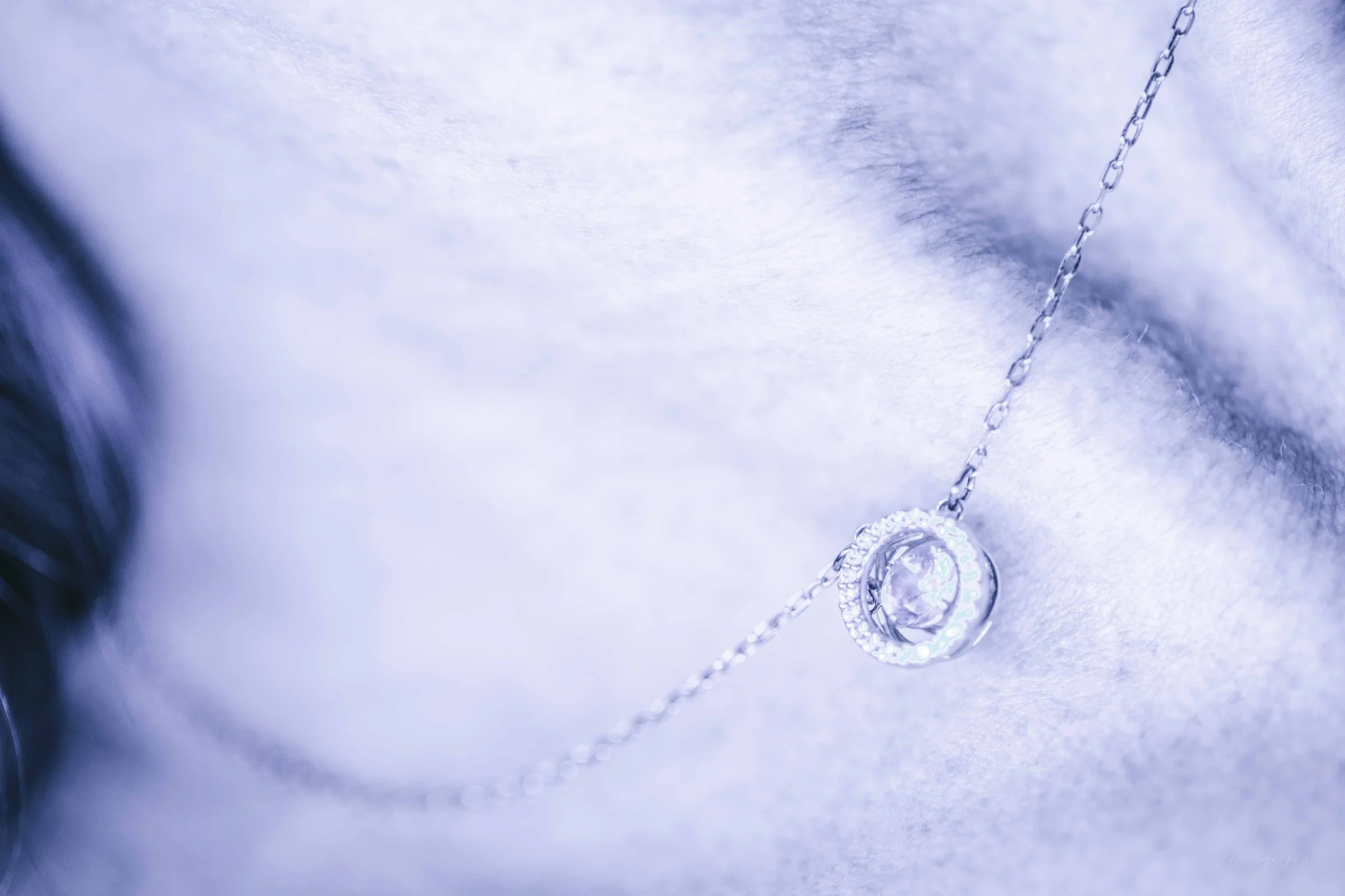 Un pendentif en forme de cercle avec un petit diamant au centre, suspendu à une chaîne en argent, posé sur un tissu blanc ou argenté.