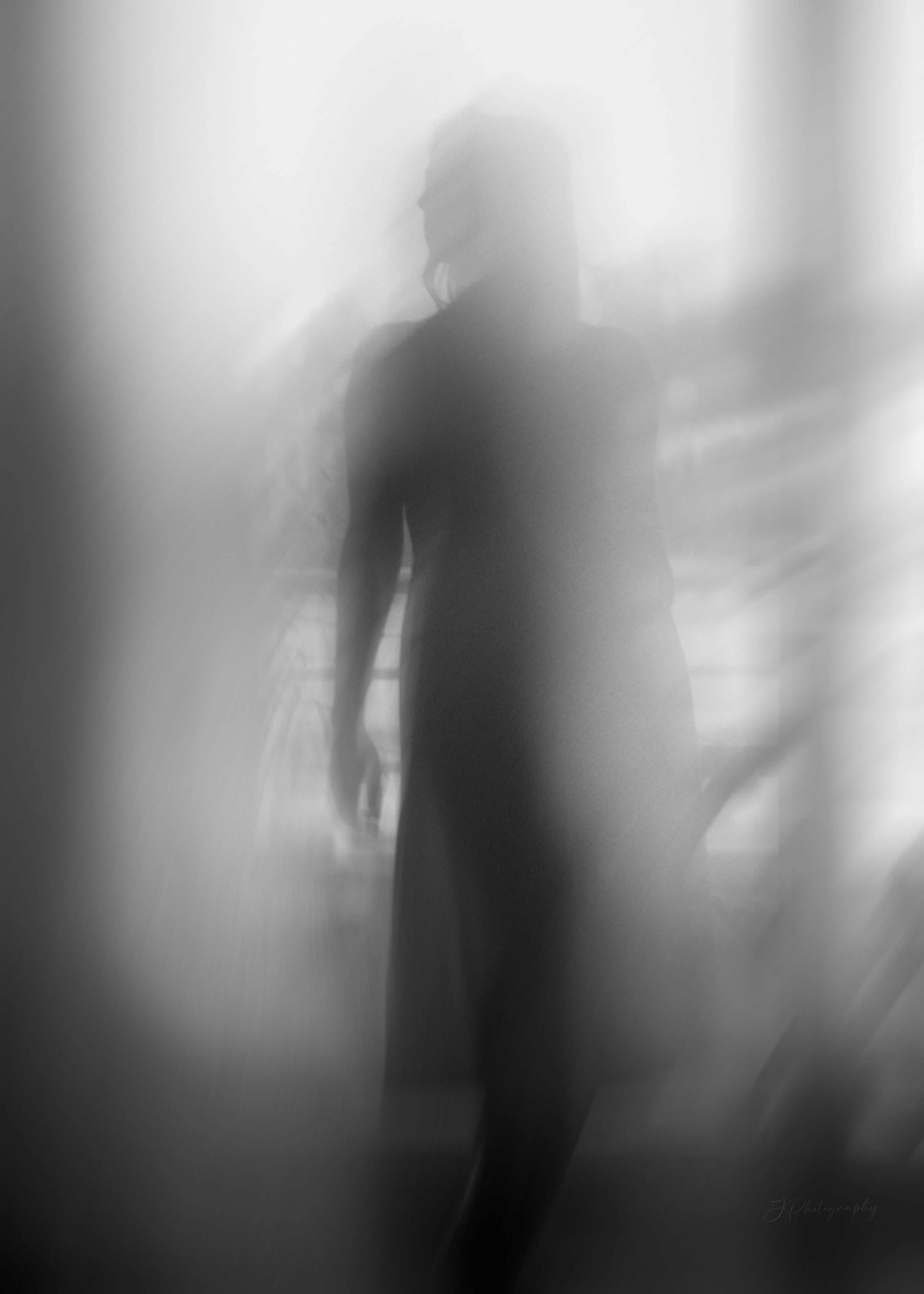 Silhouette floue d'une femme en robe, vue à travers une surface translucide ou brumeuse, avec un arrière-plan indéfini.