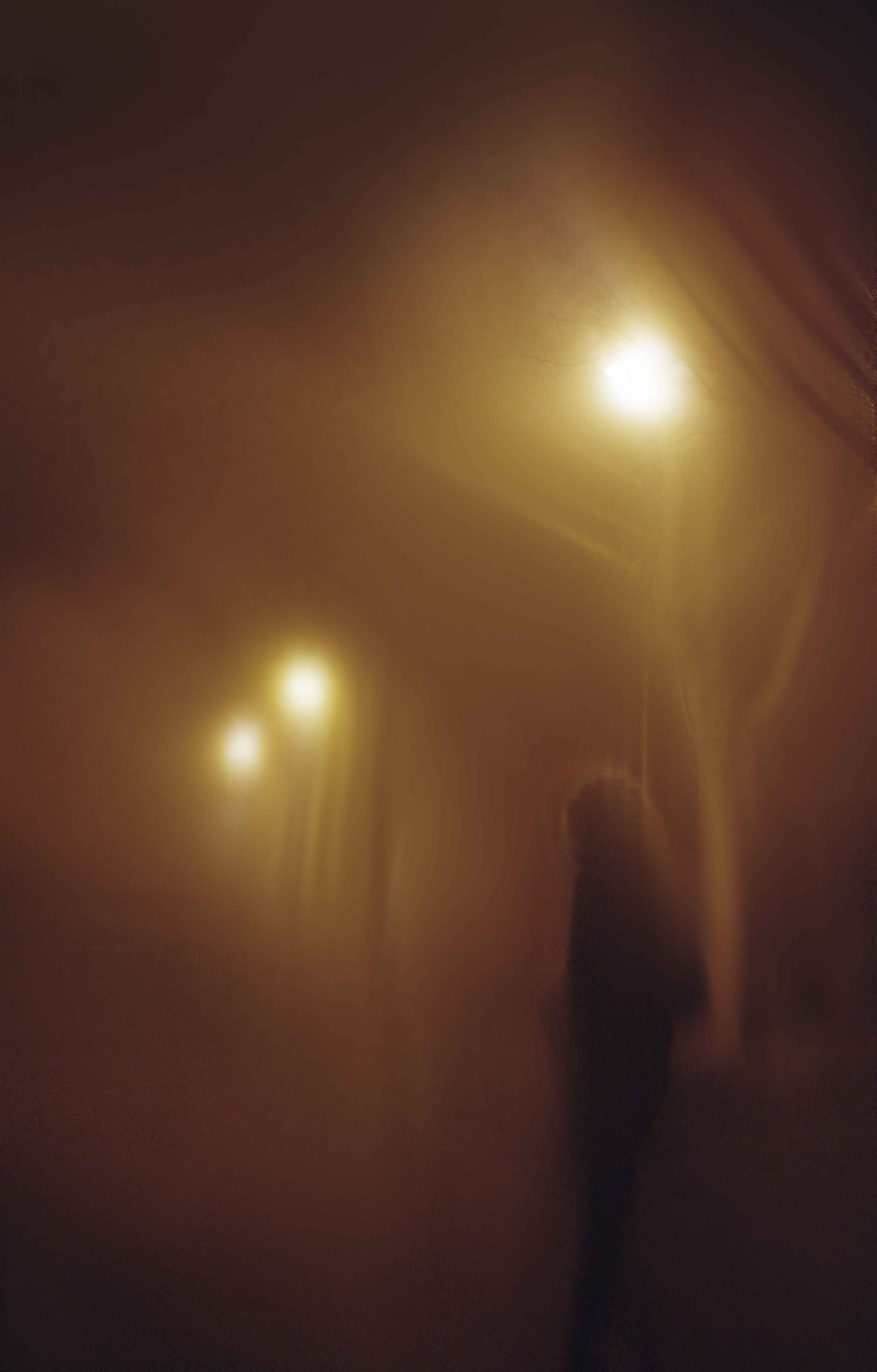 Une personne en perspective, silhouette vue à travers une vitre ou une surface translucide, avec des lumières jaunes ou dorées en arrière-plan.