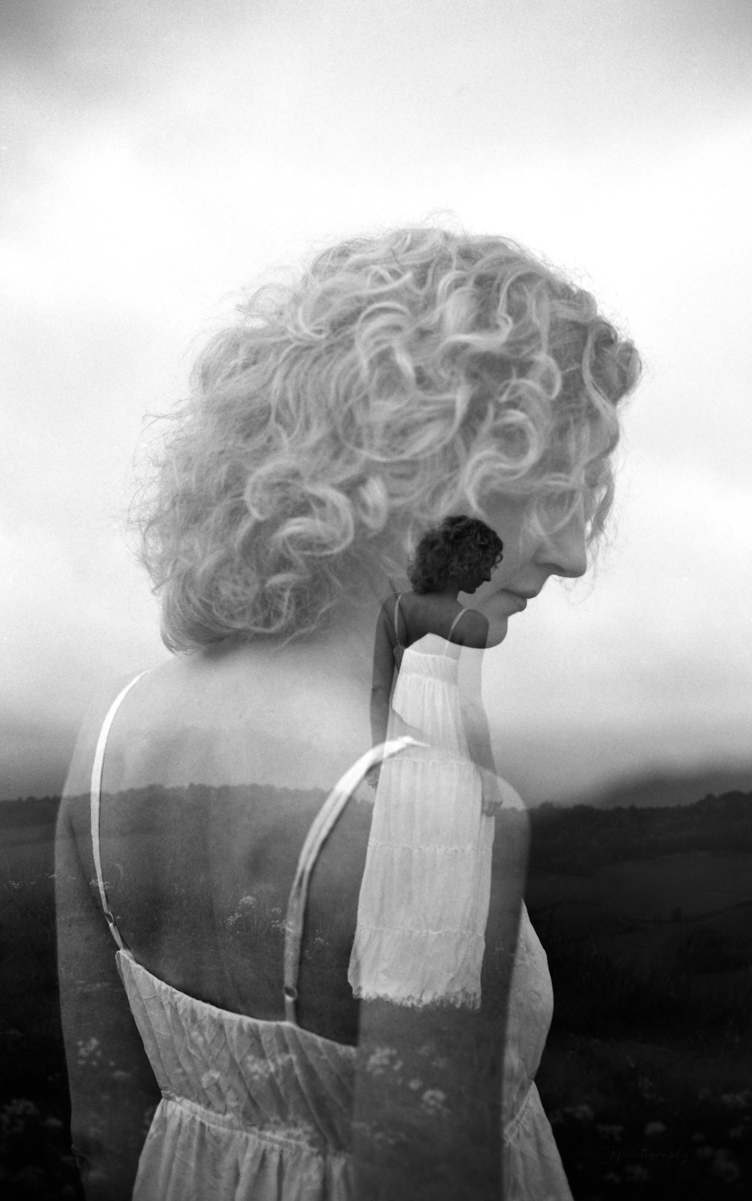 Une double exposition en noir et blanc montrant une femme aux cheveux bouclés de profil et une autre femme en robe légère vue de dos, sur un paysage rural.