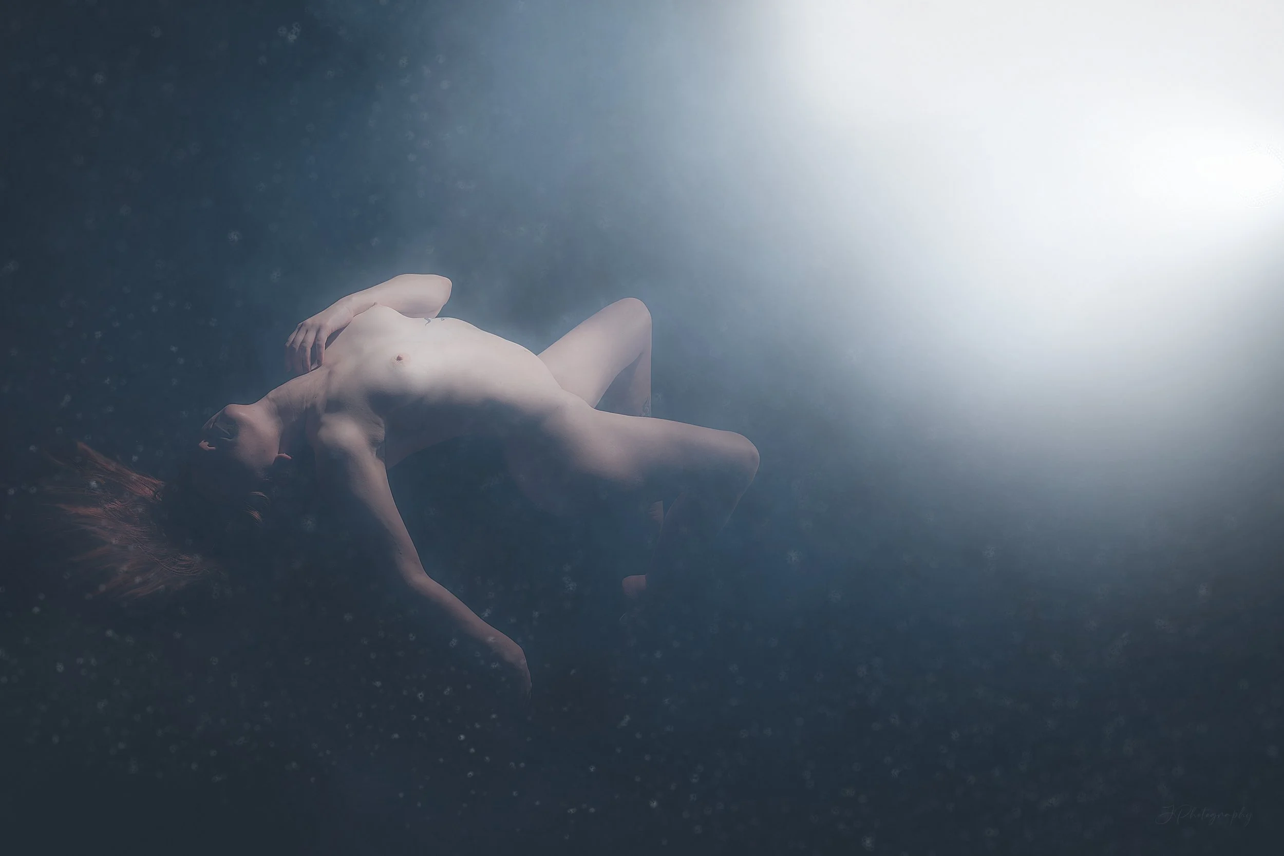 Femme nue flottant sous l'eau, éclairée par une lumière brillante.