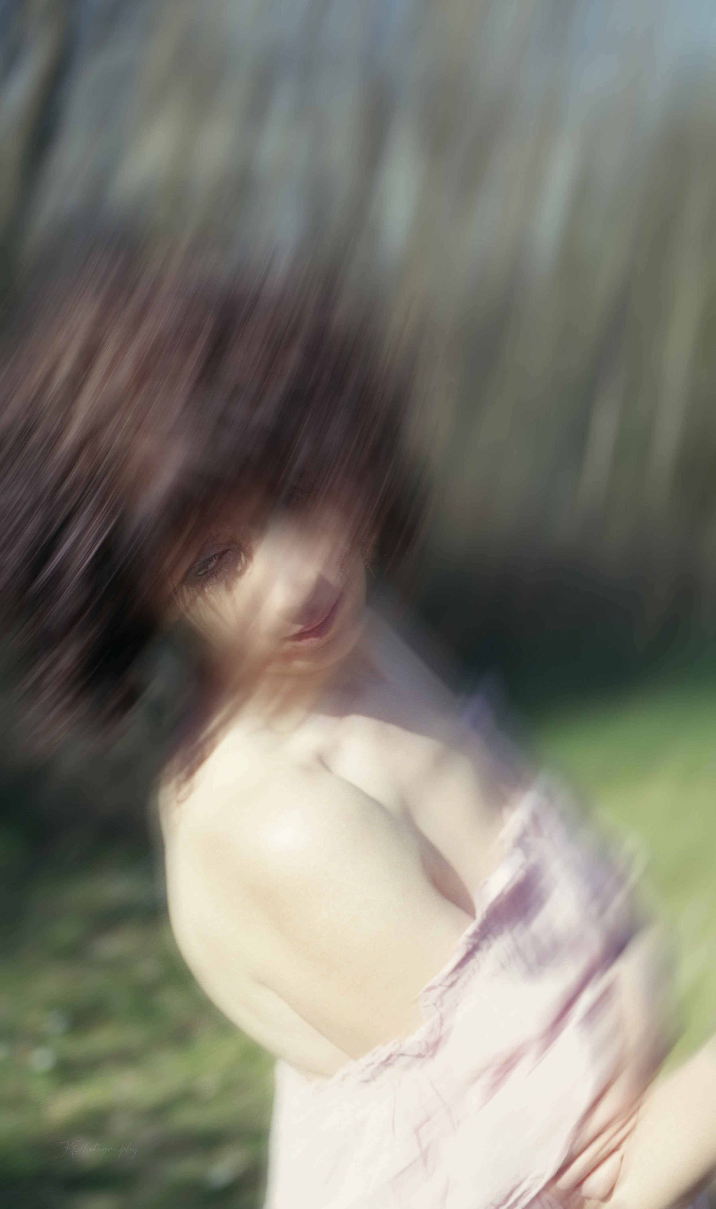 Une femme assise dehors avec un fond de végétation, l'image est floue avec un effet de mouvement et de flou artistique.