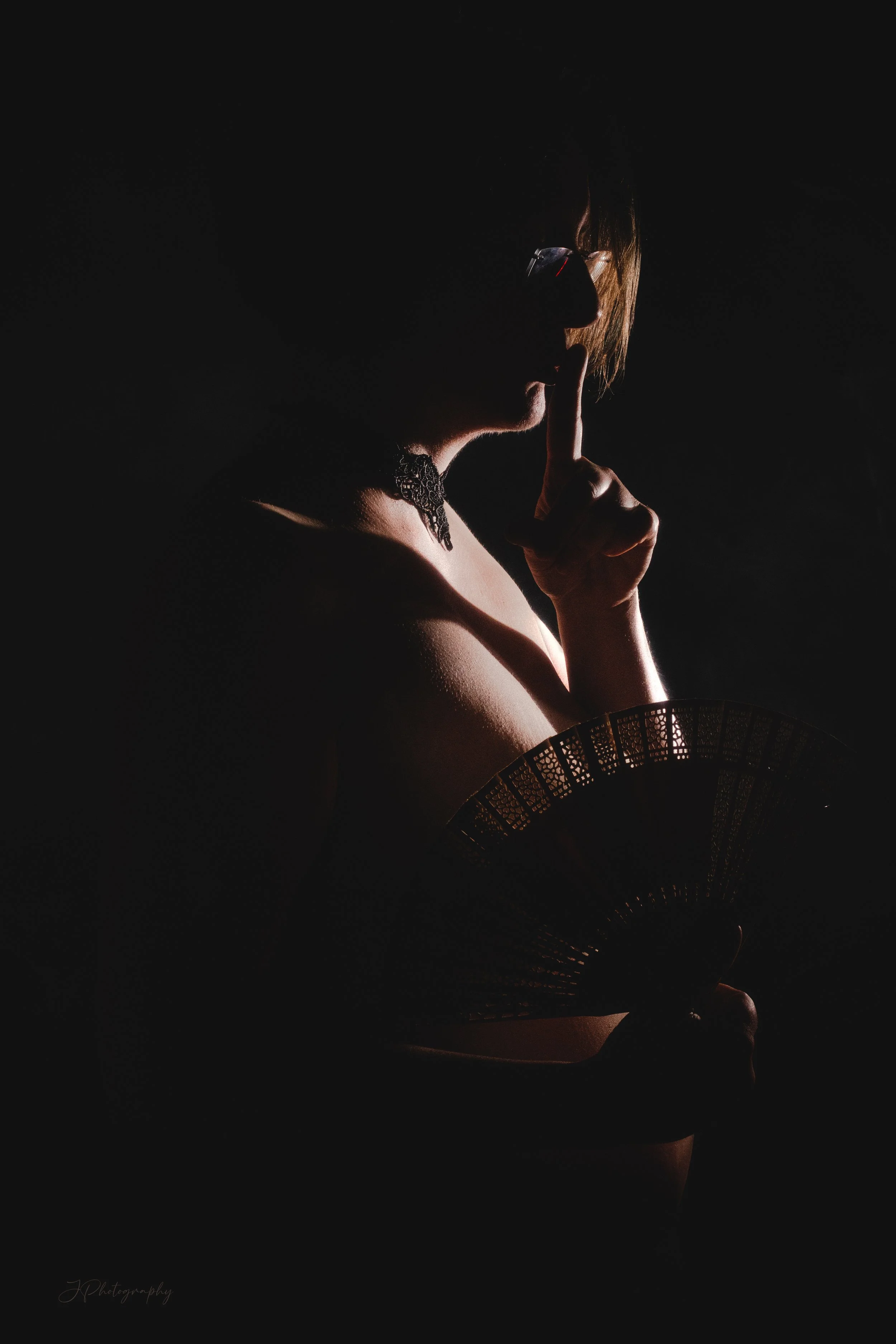 Silhouette d'une femme tenant un éventail et faisant un geste de silence avec son doigt sur ses lèvres, ambientée dans une lumière tamisée