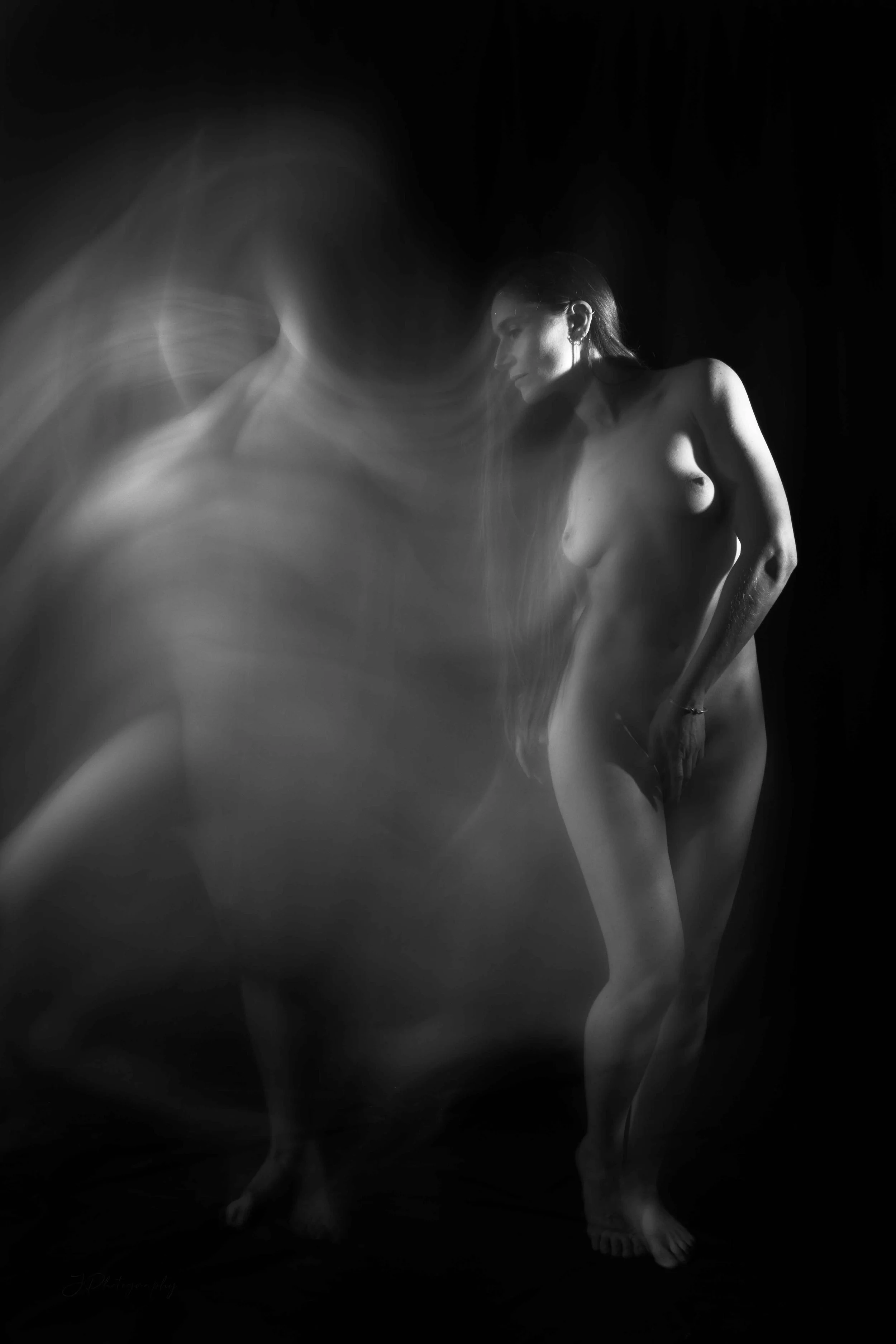 Une photo en noir et blanc d'une femme nue, avec un effet de flou ou de mouvement autour d'elle.