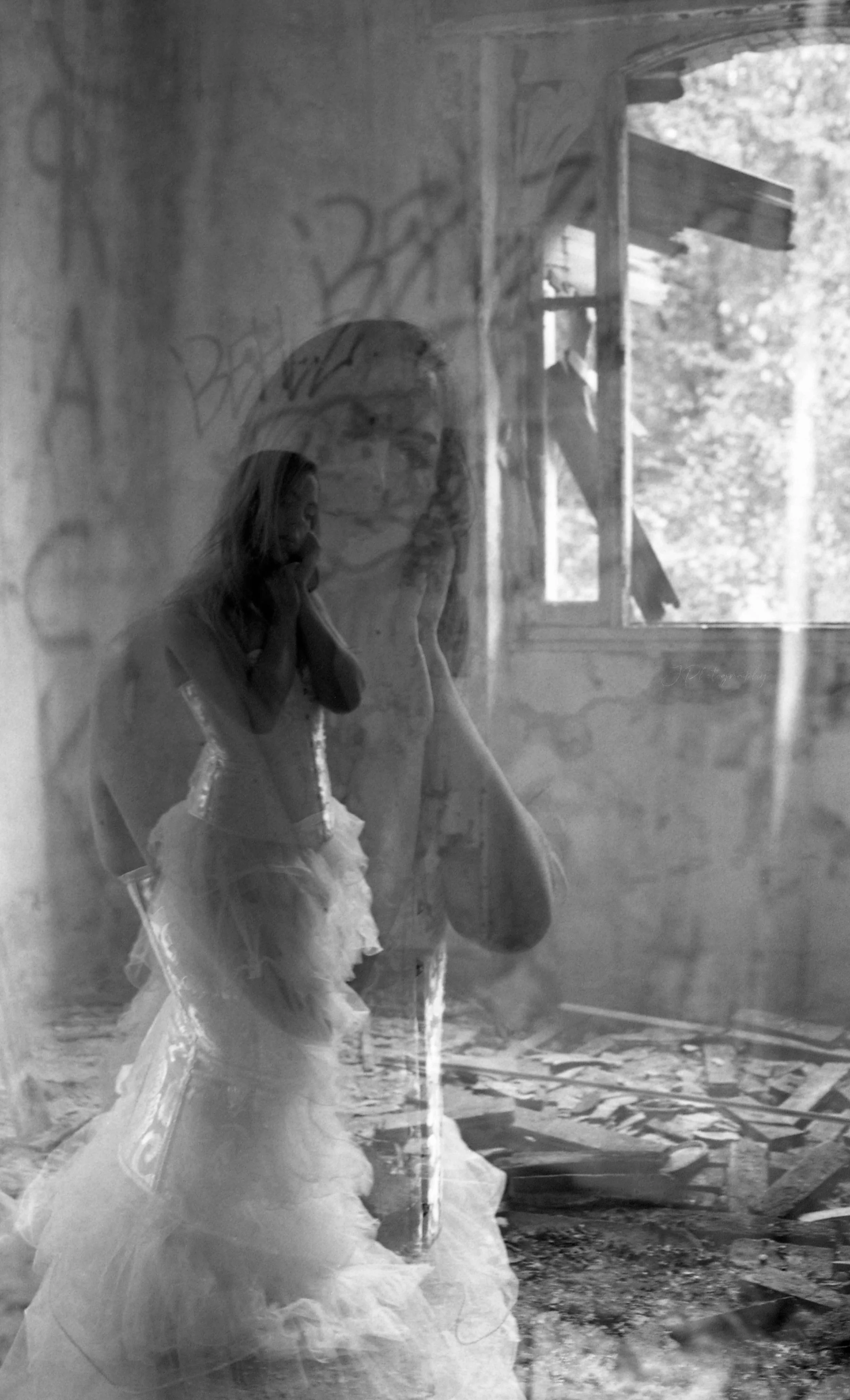 Double exposition argentique. Reflet d'une femme portant une robe de mariée dans une fenêtre, avec un décor en ruine et un arbre visible à l'extérieur.