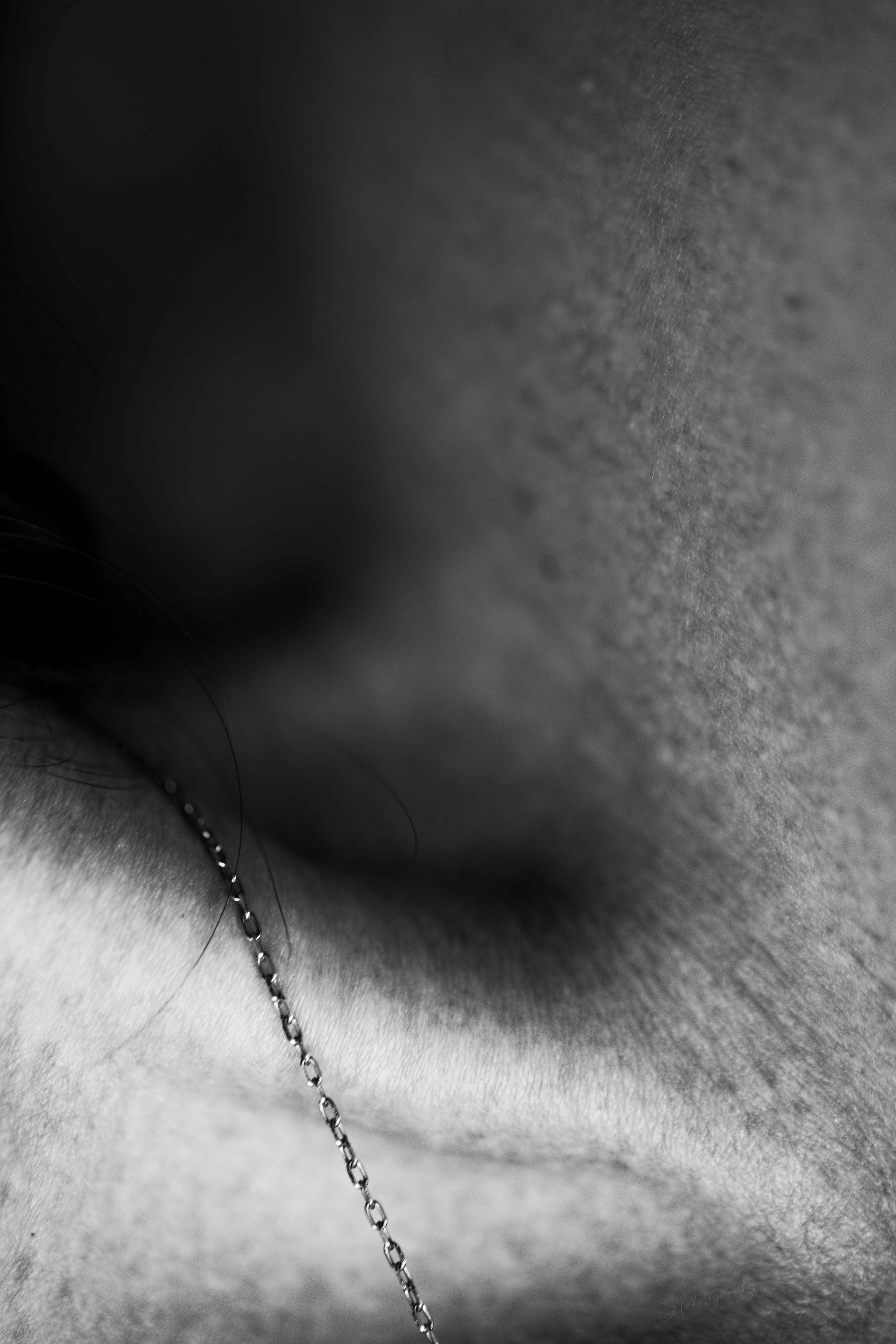 Photo en gros plan d'une zone de peau humaine avec un piercing et une chaîne autour du piercing. Image en noir et blanc.
