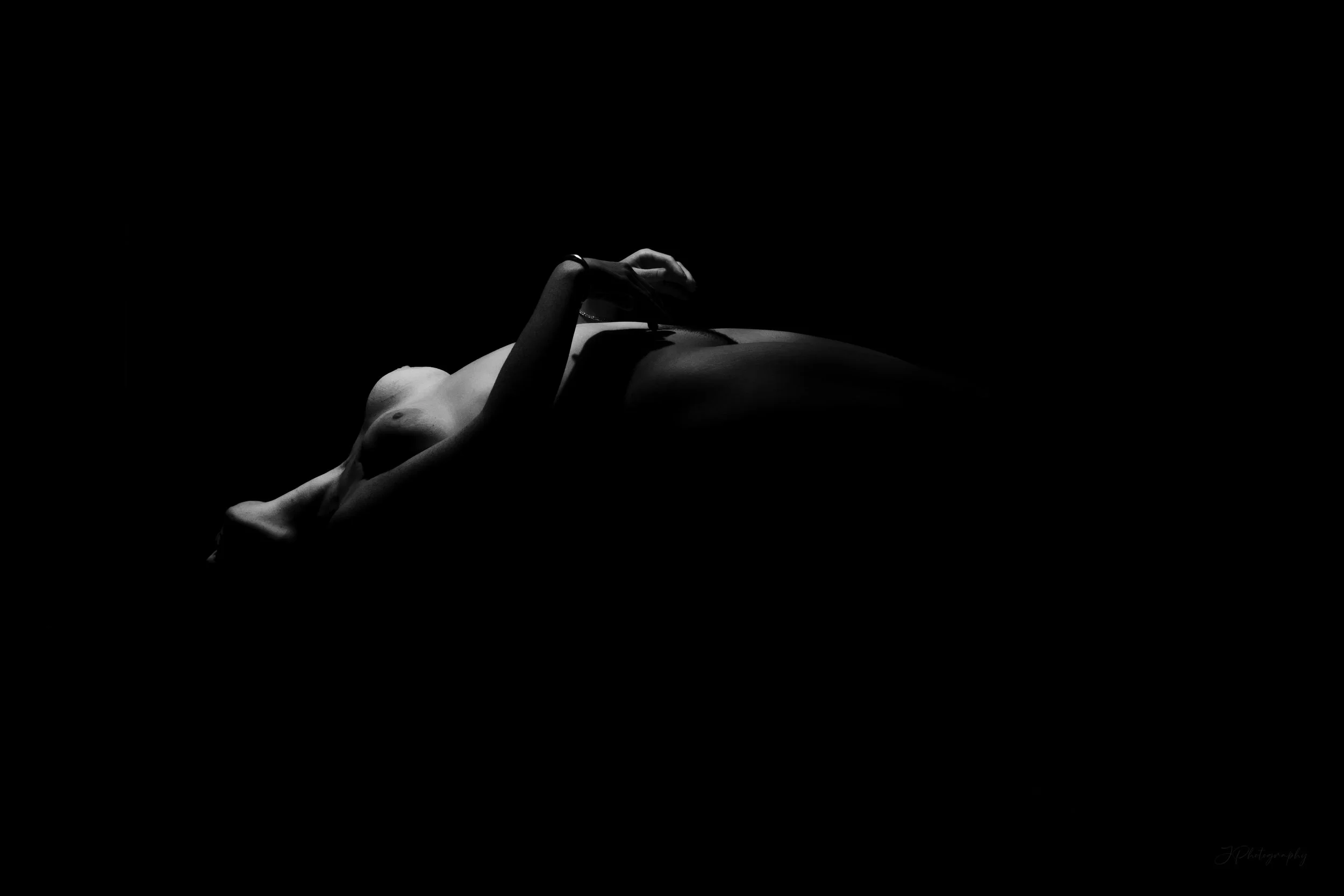 Photo en noir et blanc d'une silhouette de femme allongée, avec une lumière douce qui met en valeur ses formes et crée un contraste avec l'arrière-plan sombre.