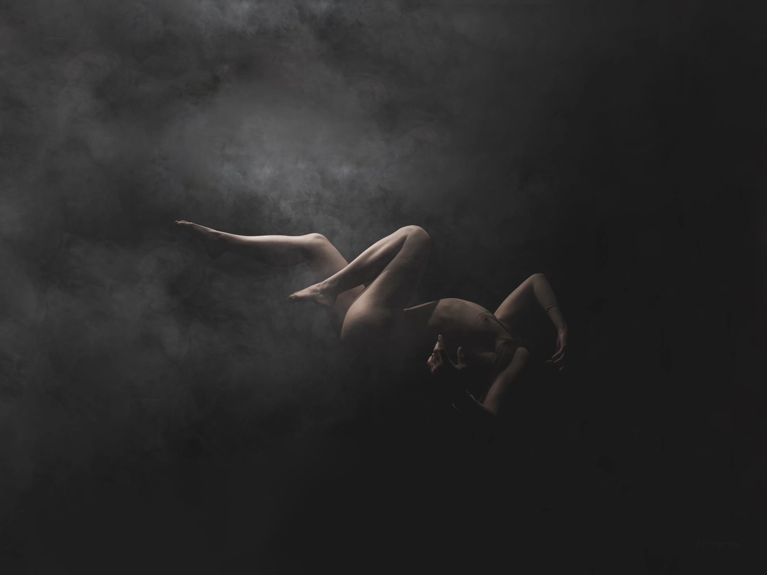 Une femme nue allongée dans une ambiance sombre et brumeuse, avec un éclairage doux créant une atmosphère mystérieuse et artistique.