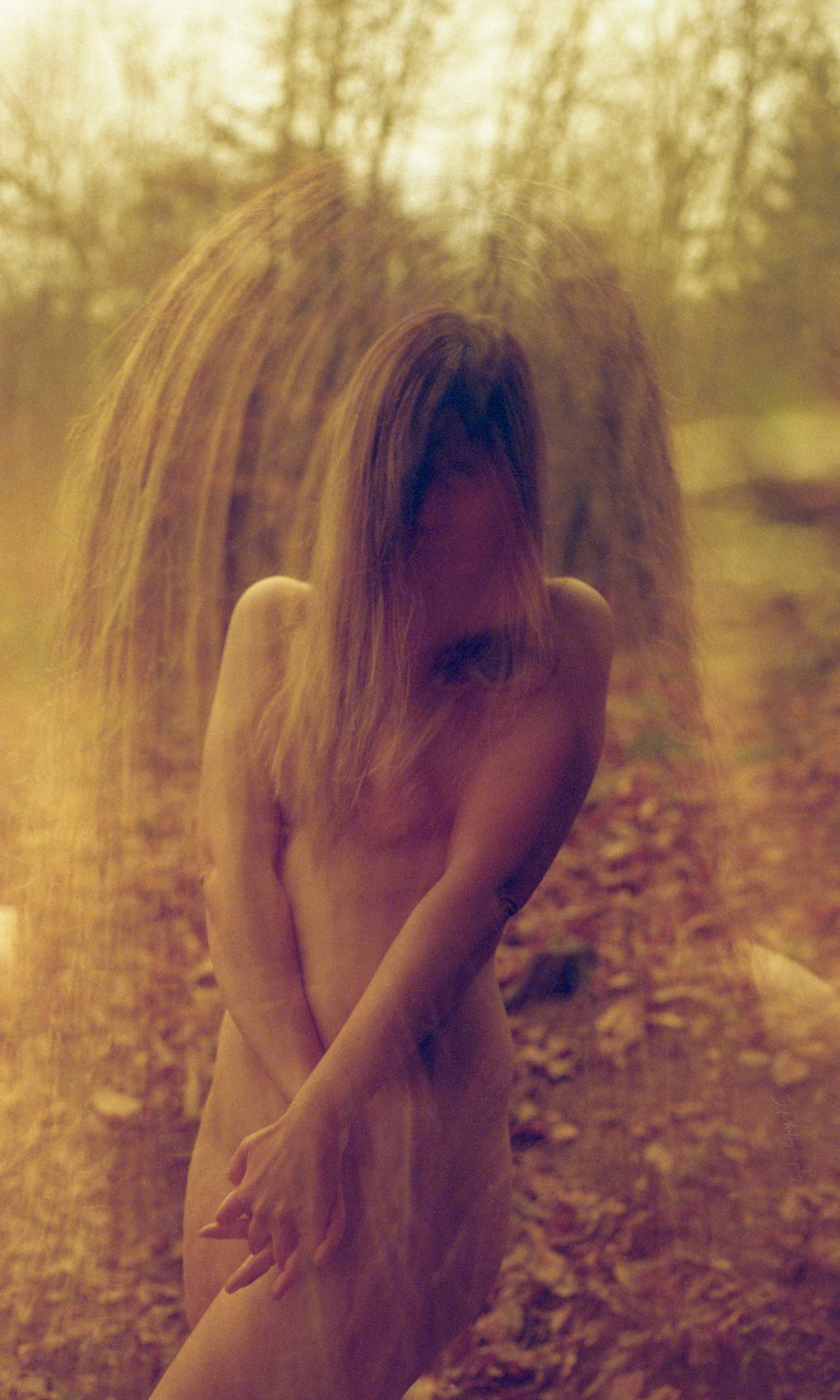 Une femme nue avec de longs cheveux roux se tenant dans une forêt, avec un effet de double exposition ou superposition d'images.