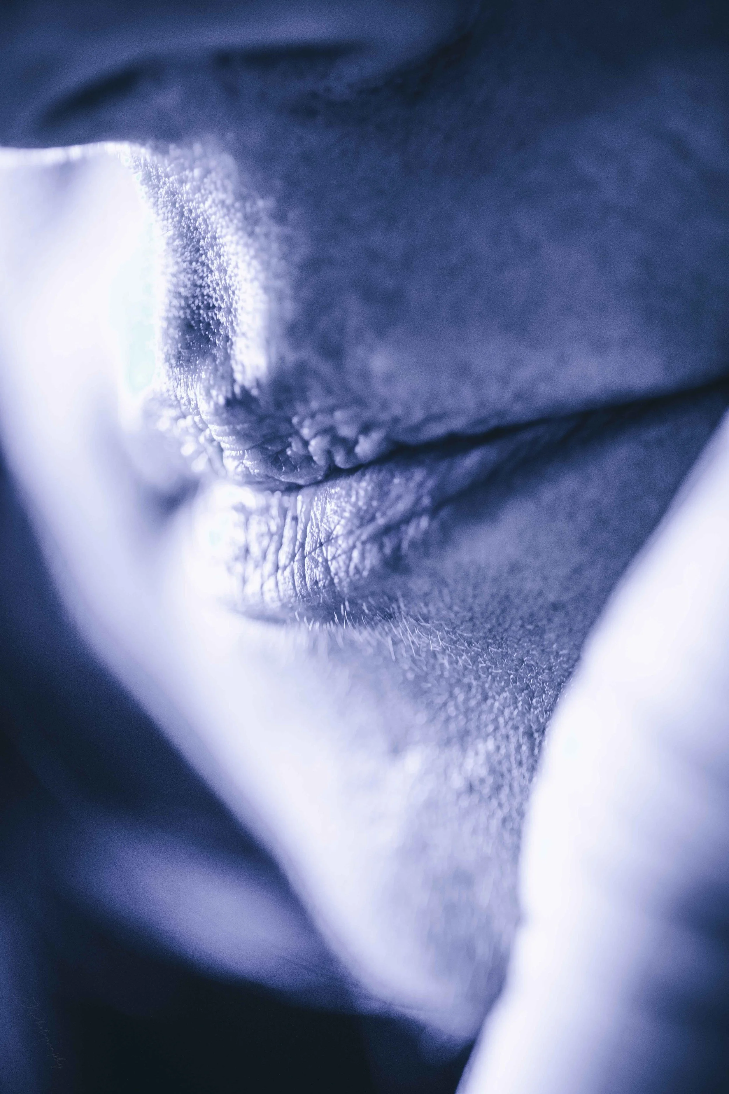 Un gros plan d'une personne à la peau claire, photographié en gros plan avec un effet artistique, mettant en évidence la texture de la peau, notamment les lèvres et le contour du visage.
