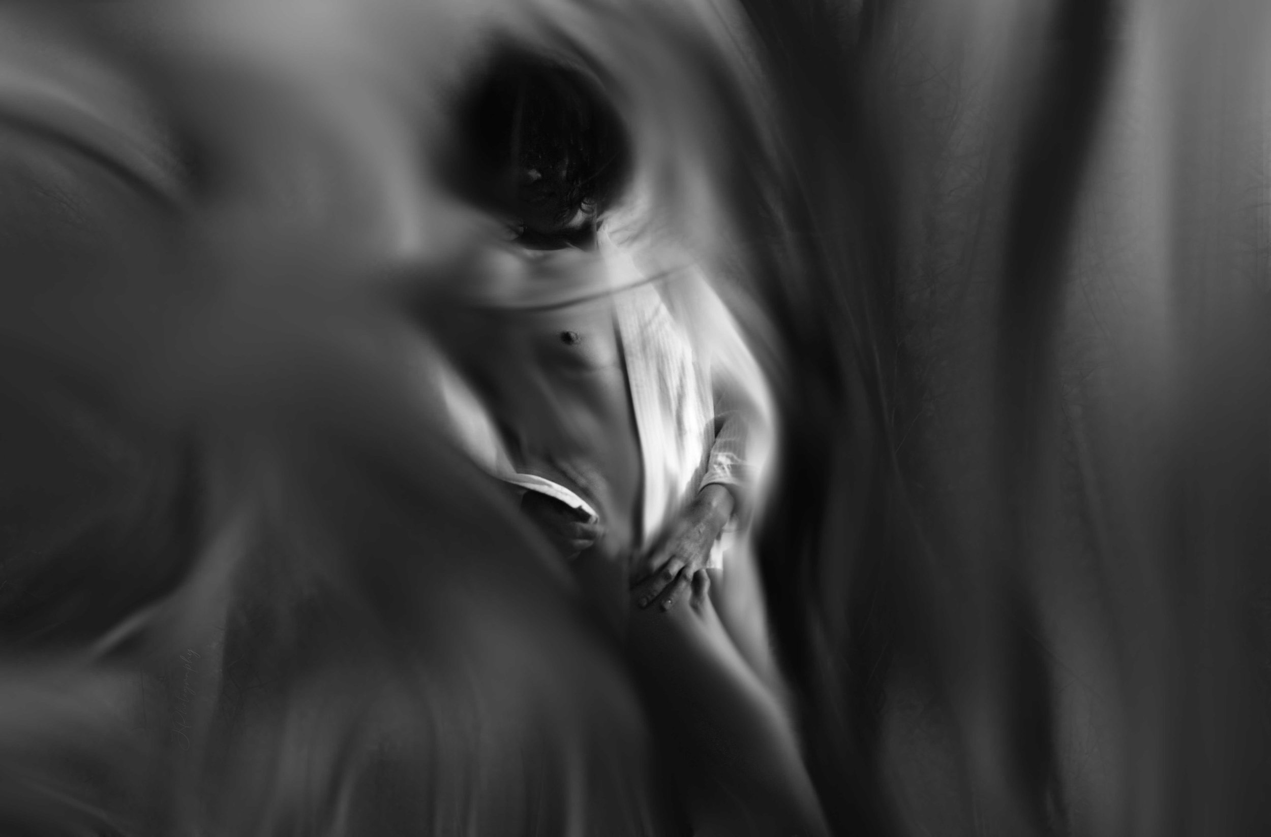 Photo en noir et blanc d'une personne habillée en blanc, vue à travers une surface déformée, créant un effet flou et magnifique.