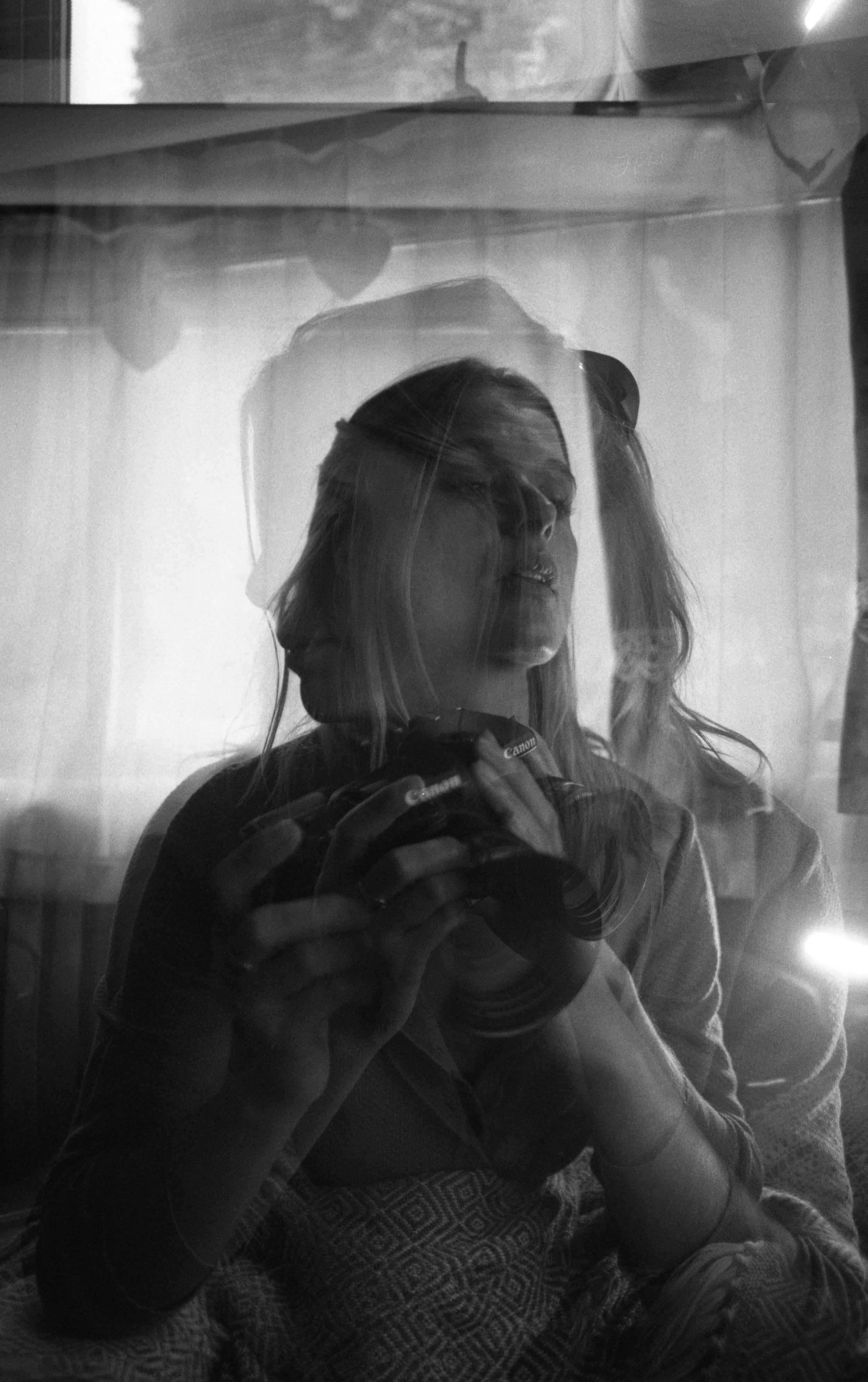 Reflet en noir et blanc d'une femme prenant une photo avec un appareil Canon, vue à travers une surface réfléchissante.