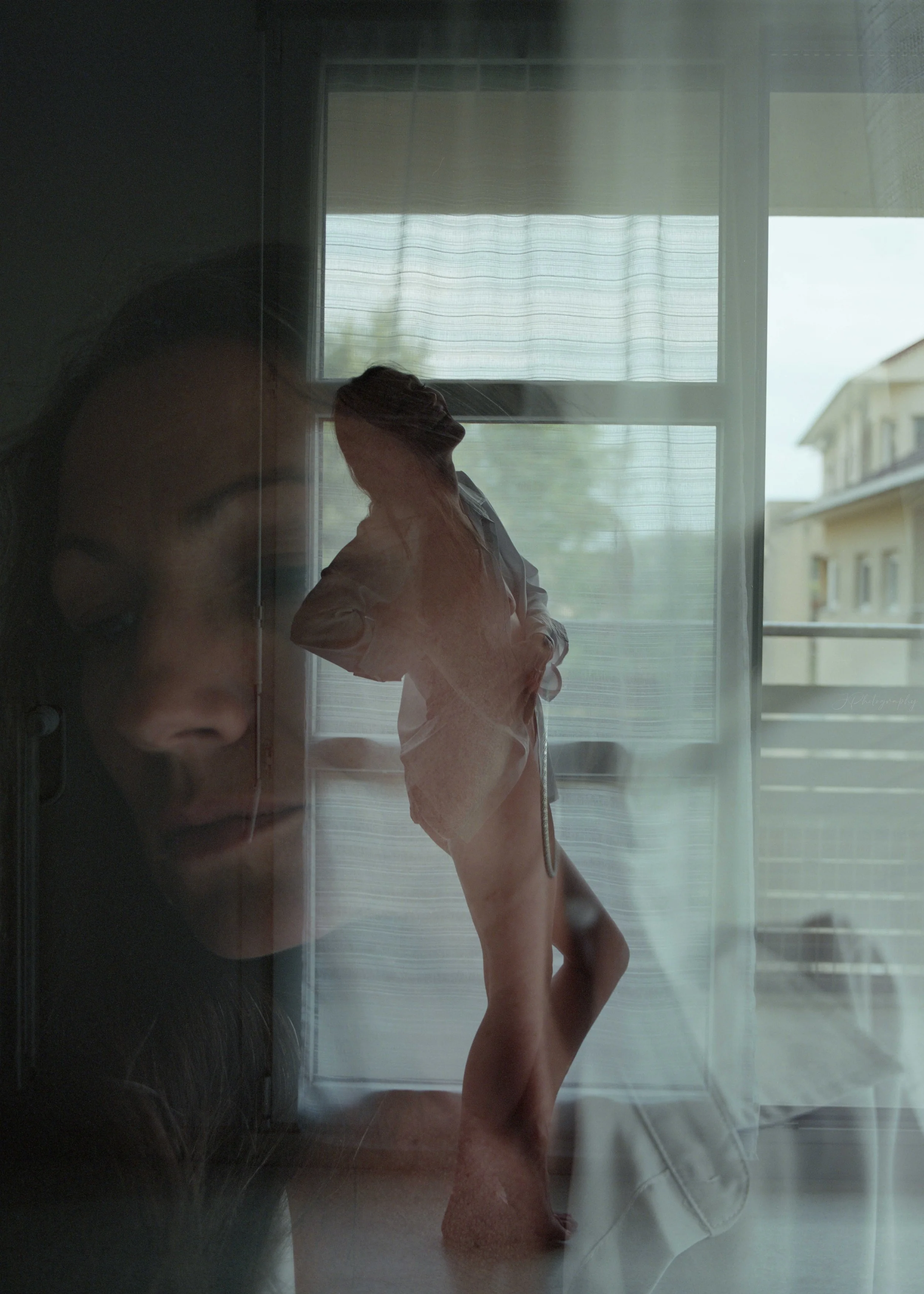 Une double exposition photographique montrant le visage d'une femme en gros plan à gauche et une femme debout près d'une fenêtre avec des rideaux à droite.