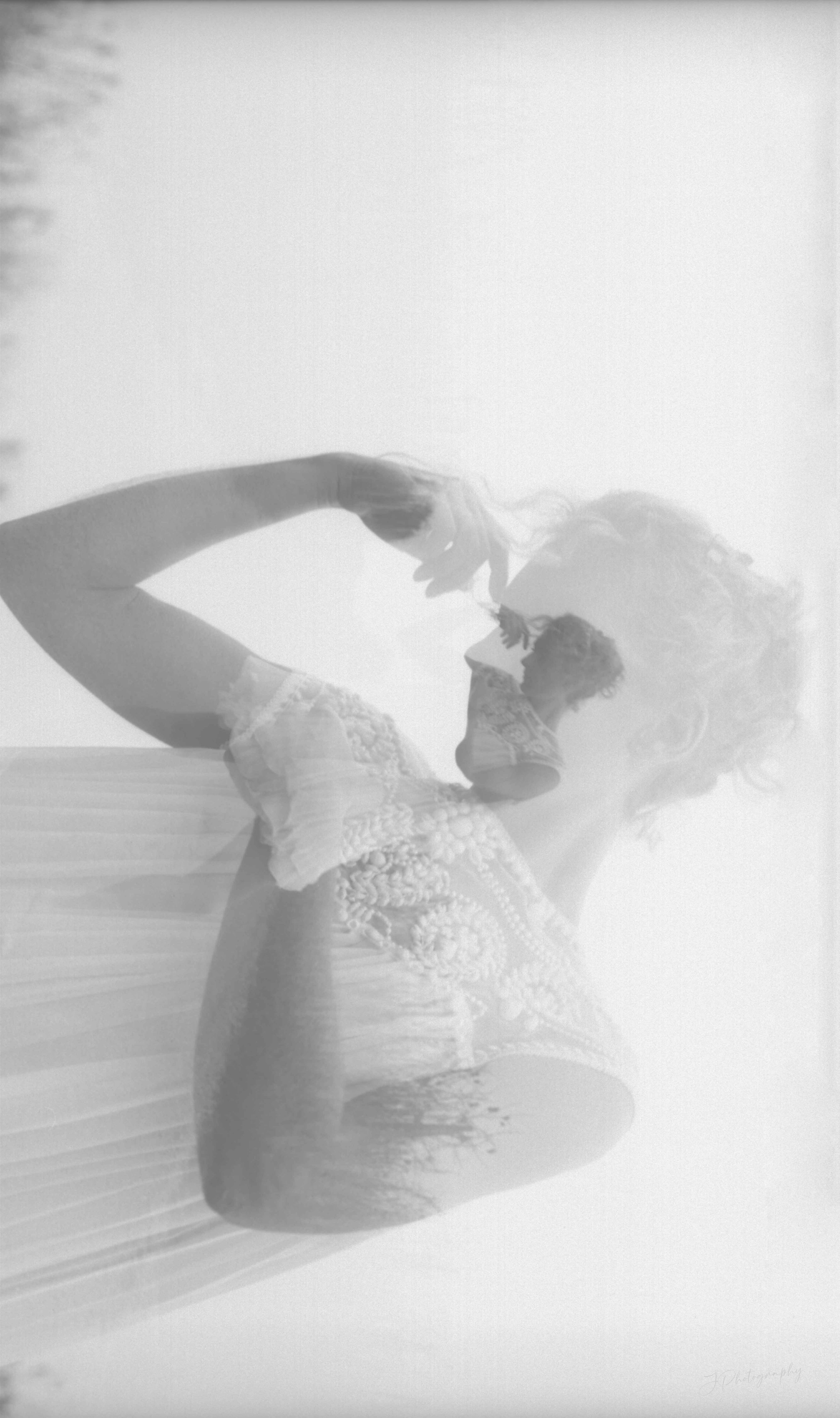 Double exposition argentique. Une femme portant une robe brodée, vue en reflet, avec un fond flou et un effet de double exposition.