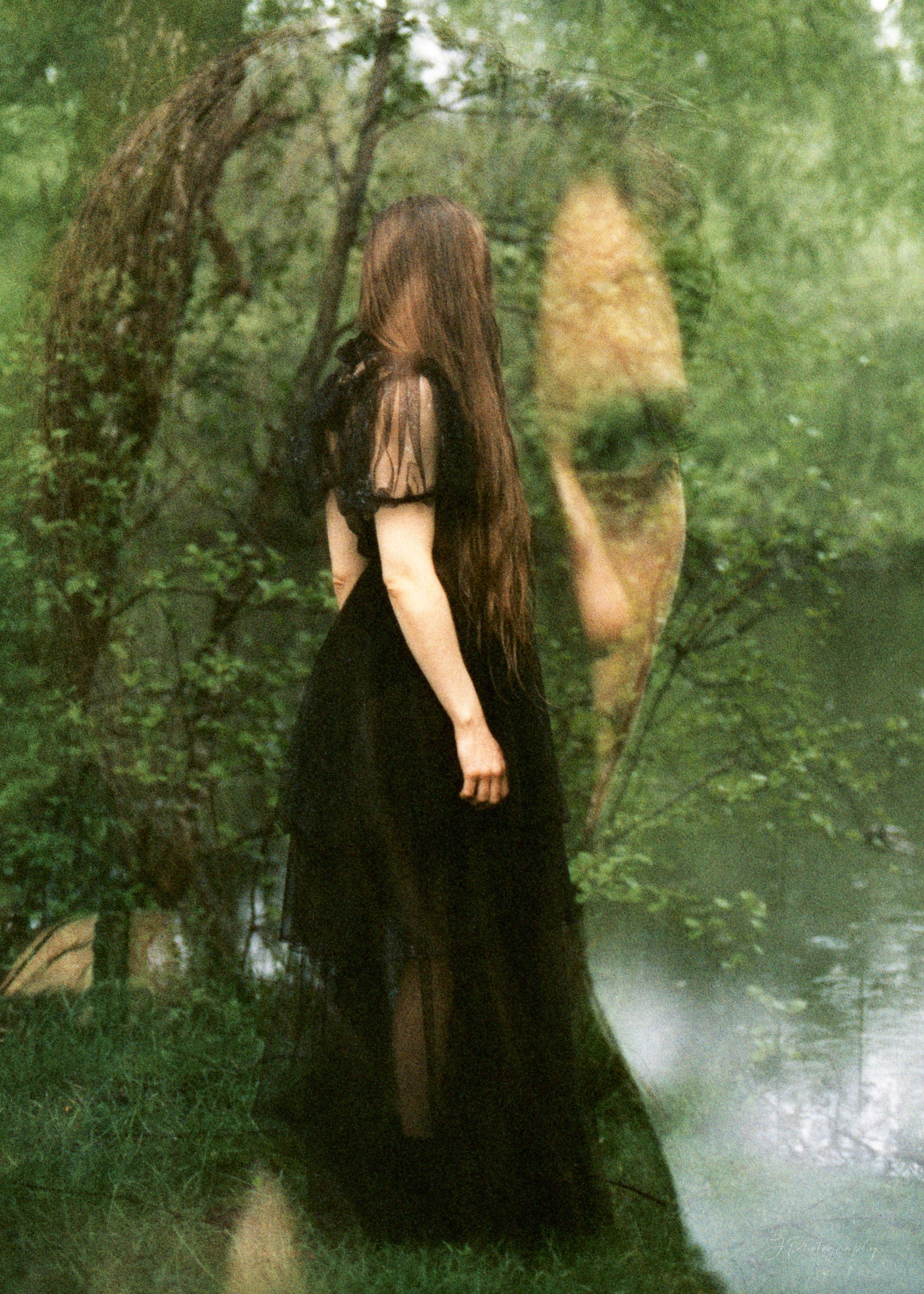 Une femme en robe noire dans une forêt verte, avec un reflet mystérieux de son visage dans une surface liquide ou miroir.